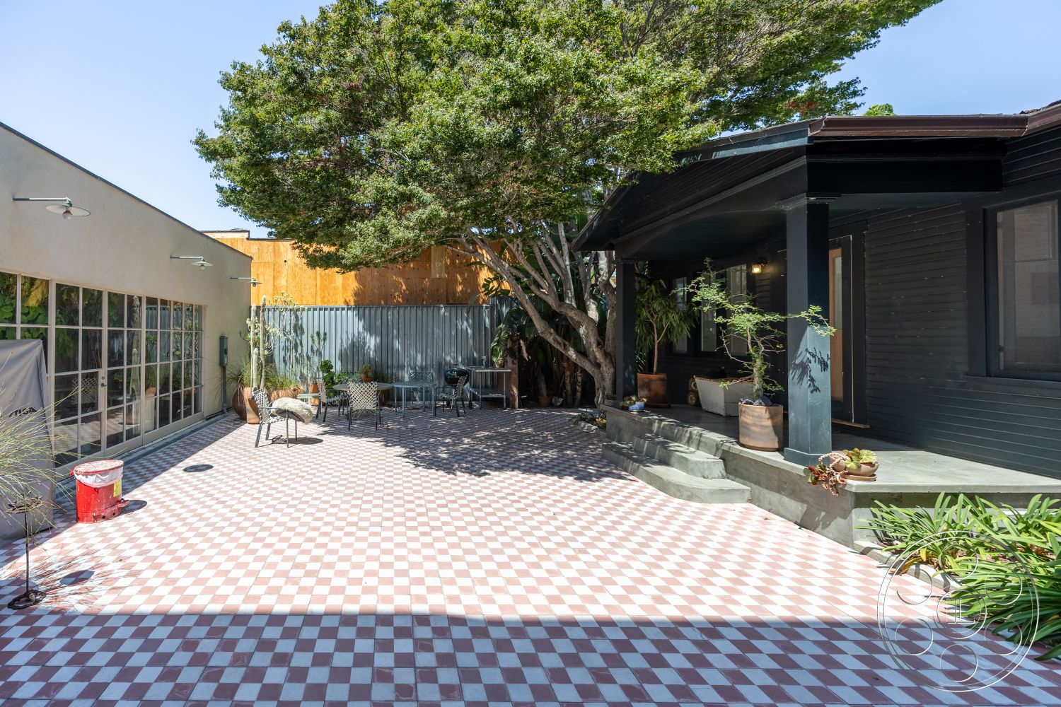 Studio 100 - urban setting, outdoor dining area, landscaped backyard, modern architectural style, exterior concrete steps, exterior potted plants, exterior glass windows, exterior patio flooring - checkered tile floors, exterior raised garden beds, exterior wood beam porch ceiling, exterior natural tree shade, exterior metal fence, courtyard home layout, sunlit patio area