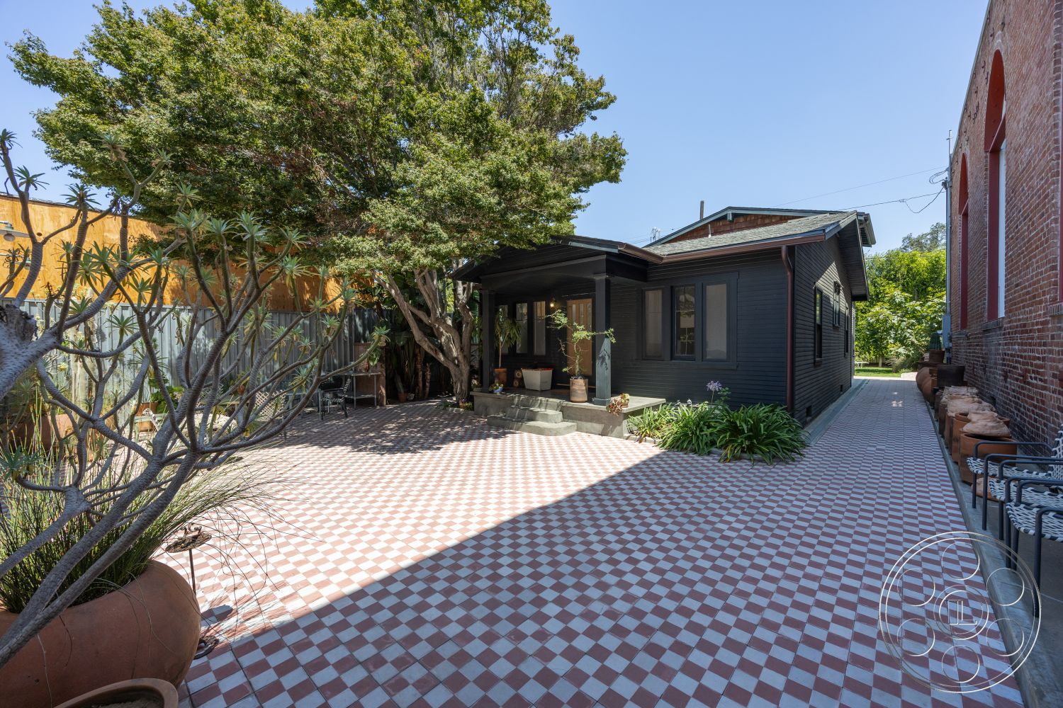 Studio 100 - exterior, outdoor seating area, urban setting, sloped roof, dark wood paneling, landscaped garden patio, built-in planter boxes, traditional home, red and white checkered tile patio flooring, mature trees in garden, sidewalk with stone border, decorative clay pots