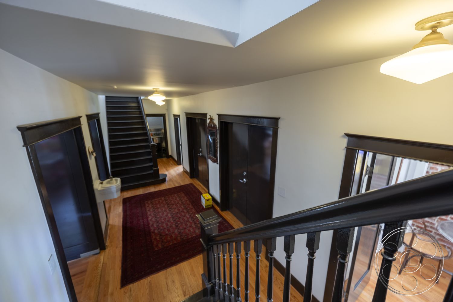 Studio 100 - arched doorways, red area rug, recessed ceiling lights, natural light from skylight, traditional home design, white painted walls, exposed brick accent wall, black metal stair railing, hardwood foyer flooring, dark wood interior doors, two-story staircase, open concept entryway