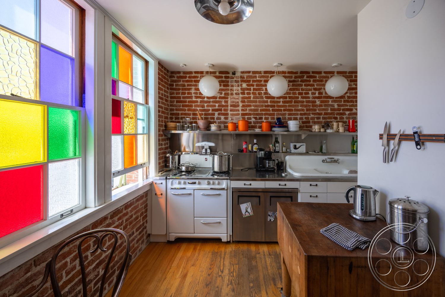 Studio 100 - minimalist decor, stainless steel appliances, modern pendant lighting, metal shelving units, white cabinetry, functional kitchen space, natural light from windows, open kitchen layout, hardwood kitchen flooring, exposed brick kitchen wall, contemporary kitchen island, bright and airy interior, colorful stained glass windows, industrial kitchen details, small urban kitchen