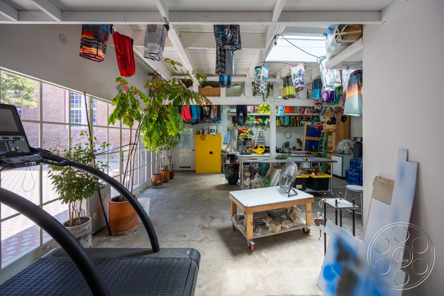 Studio 100 - natural light, open floor plan, potted plants, workshop area, concrete flooring, large glass windows, industrial style, creative studio, functional workspace, exposed wood ceiling beams, indoor garden space, yellow storage cabinet, textile storage, modern treadmill, multi-use interior, artistic display area