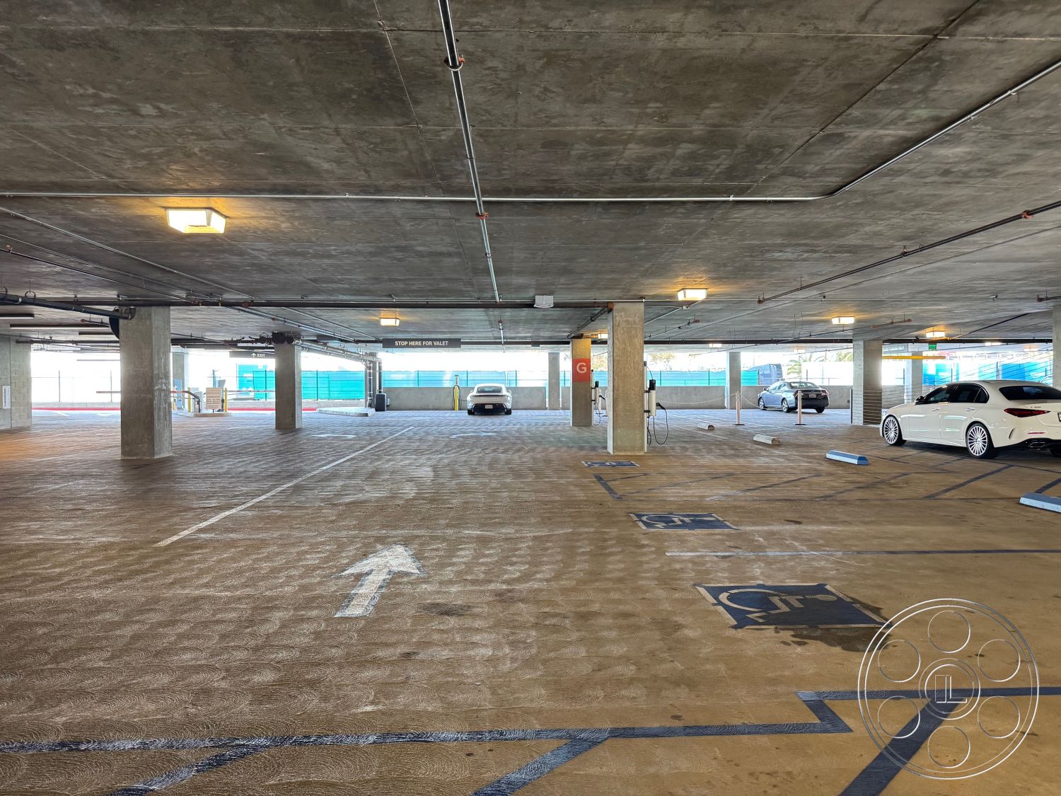 Office 121 - contemporary design, industrial lighting fixtures, exposed concrete ceiling, smooth concrete floors, textured concrete surface, steel support columns, concrete parking structure, marked parking spaces, open parking layout, glass exterior partitions, urban parking environment, interior parking garage, functional vehicle access, clear directional markings