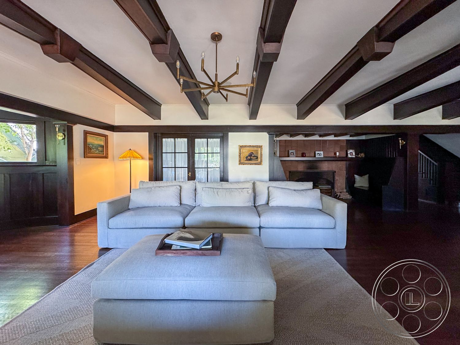 Craftsman 20 - textured area rug, open concept layout, dark wood paneling, decorative throw pillows, exposed wood ceiling beams, interior living space, hardwood living room floors, modern sectional sofa, crown molding details, chic coffee table with decor book, ambient floor lamp, traditional artwork framing, glass-paneled French doors, contemporary chandelier lighting, cozy and inviting atmosphere