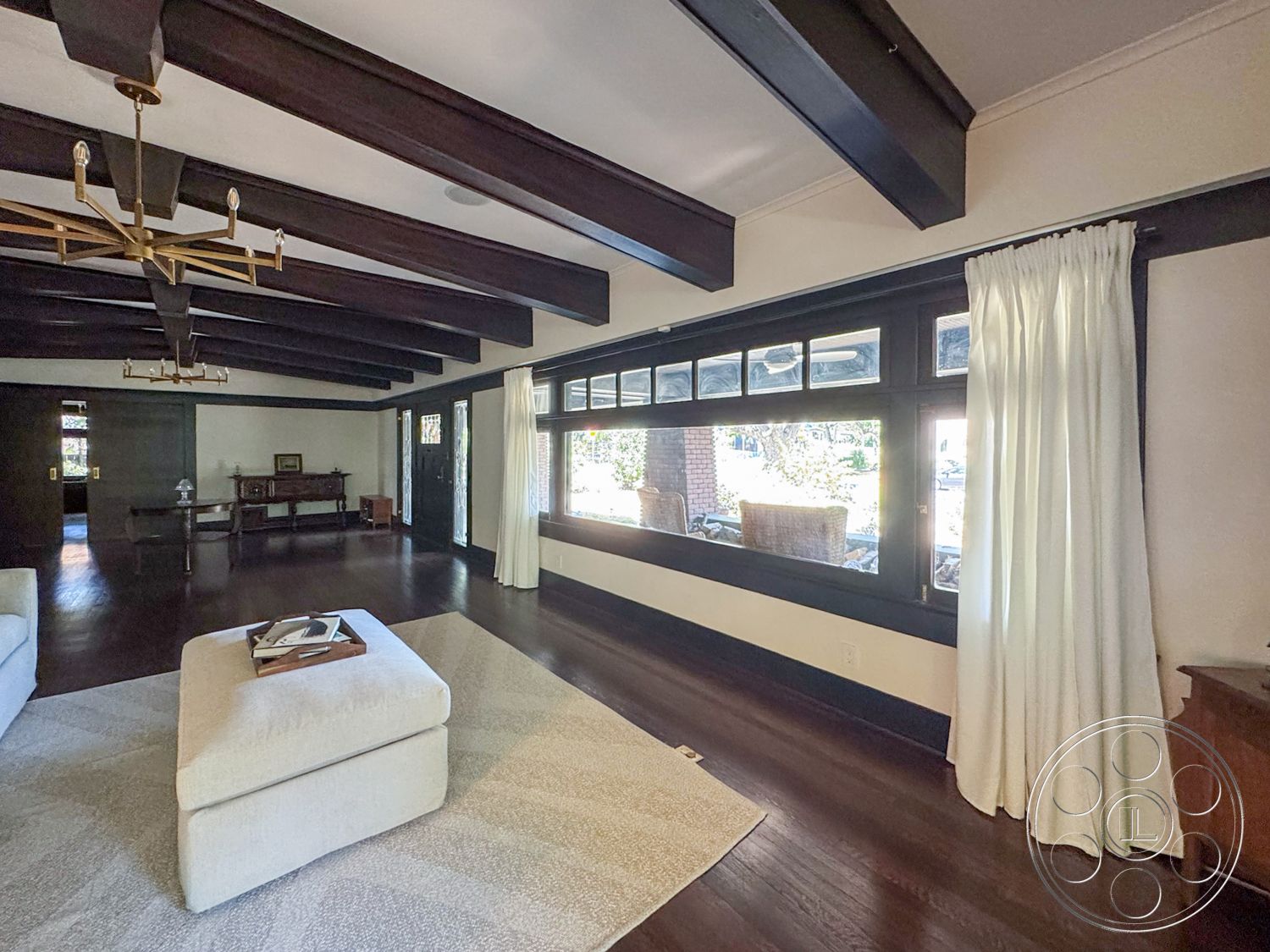 Craftsman 20 - floor-to-ceiling windows, neutral area rug, dark wood trim, exposed wood ceiling beams, hardwood living room floors, natural light-filled space, stone fireplace surround, modern chandelier lighting, traditional crown molding details, white fabric curtains, built-in wooden sideboard, spacious open interior, traditional American Craftsman style
