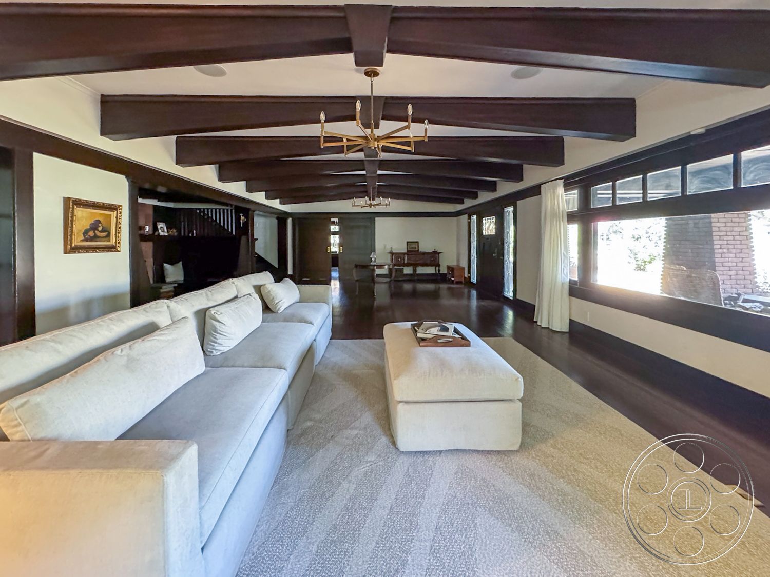 Craftsman 20 - cozy seating arrangement, neutral area rug, open concept living space, textured plaster walls, dark wood paneling, beige sectional sofa, exposed wood ceiling beams, hardwood living room floors, light-filled interior, built-in shelving units, modern chandelier lighting, framed artwork on walls, large windows with black wood trim