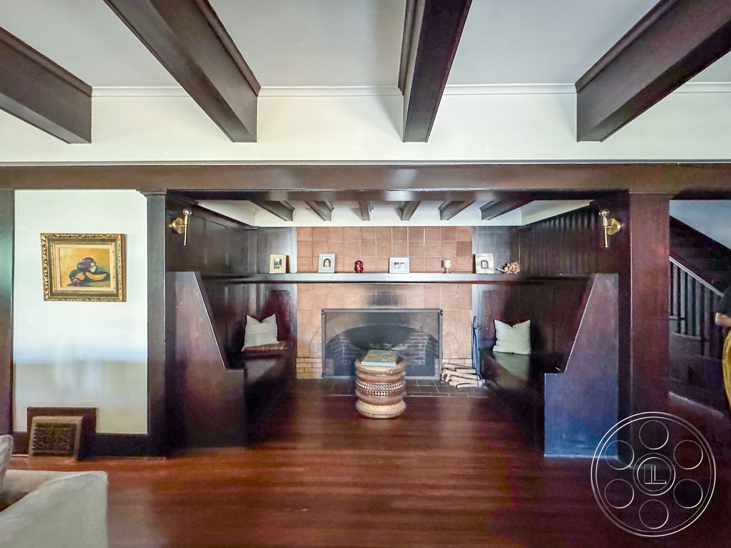 Craftsman 20 - neutral color palette, exposed wood ceiling beams, interior living space, hardwood living room floors, dark wood paneling walls, brick fireplace surround, textured plaster wall treatments, built-in wooden seating area, tiled fireplace hearth, dimensional wall art accents, room with urban cottage style, cozy seating alcoves, archway leading to staircase