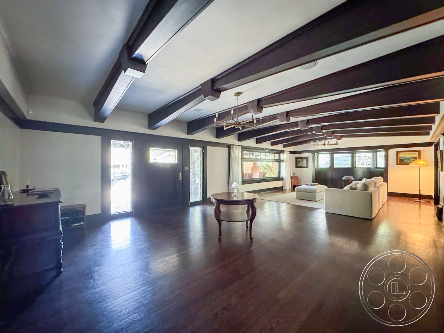 Craftsman 20 - glass entry door, exposed wood ceiling beams, hardwood living room floors, decorative molding details, white painted walls, modern sectional sofa, vaulted living room ceiling, large windows with natural light, traditional coffee table, spacious open floor plan, classic wall art decor, minimalist floor lamp