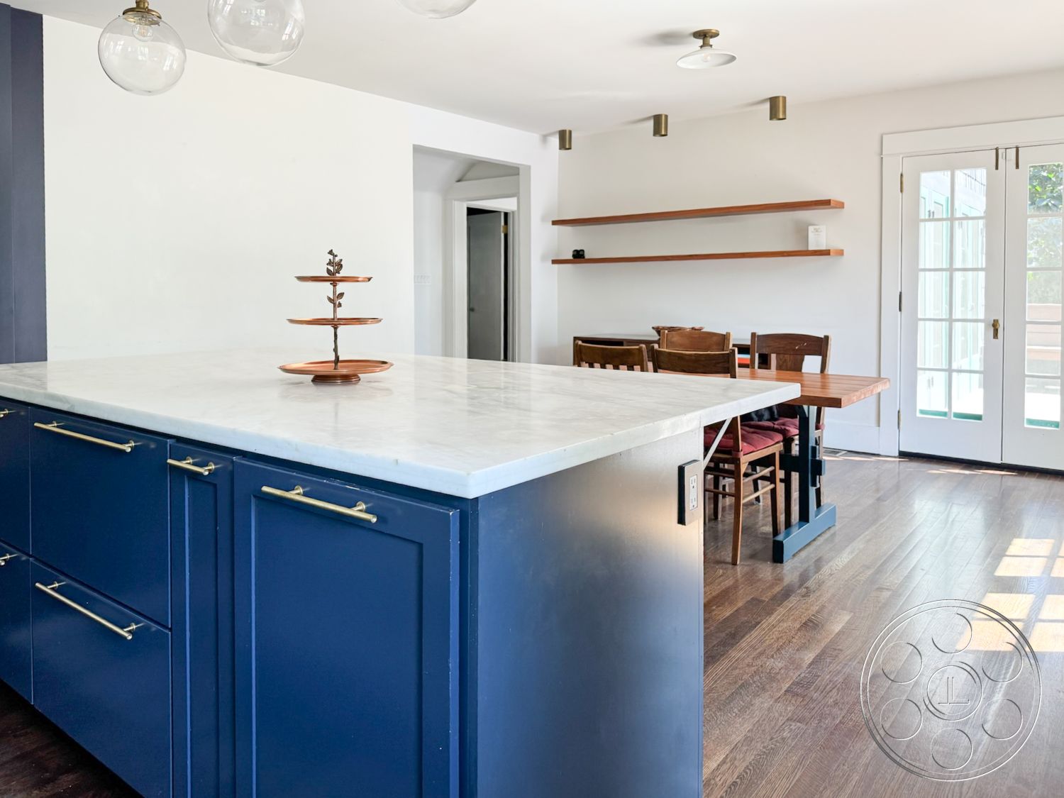 Craftsman 20 - neutral color palette, natural light, contemporary style, minimalist design, open floor plan, modern pendant lighting, wooden dining table, blue cabinetry, functional kitchen layout, wooden dining chairs, white painted walls, glass double doors, marble kitchen island, hardwood dining room floors, brass cabinet hardware, suspended wood shelves