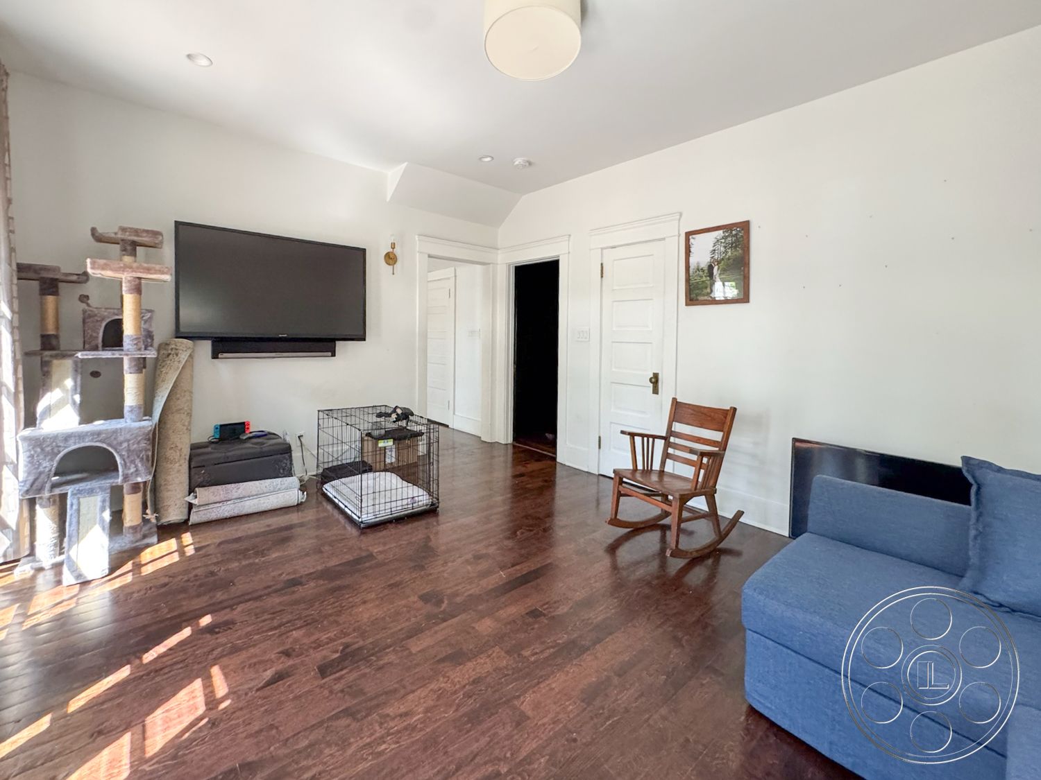 Craftsman 20 - neutral color palette, wooden accent chair, TV mounted on wall, flat ceiling, framed wall art, open living space, natural light from window, hardwood living room floors, minimalist interior design, modern sofa, white painted walls, exposed door frames, cat tree furniture, metal dog crate