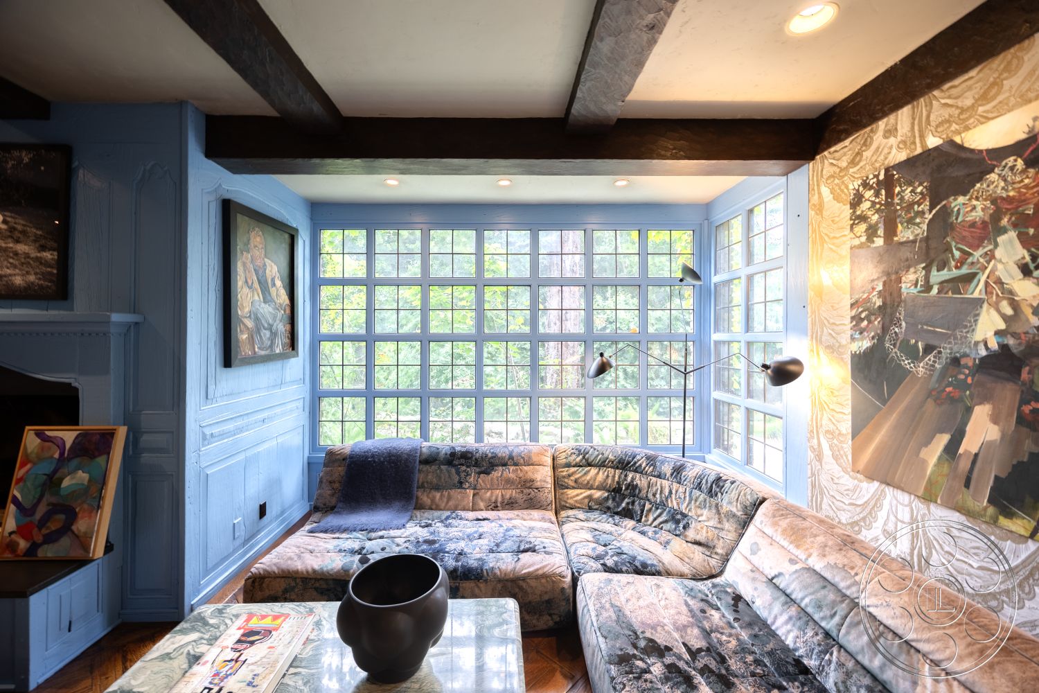 Mansion 2 - hardwood flooring, modern light fixtures, glass coffee table, artwork on walls, interior space, cozy reading nook, curved sectional sofa, textured fabric upholstery, exposed wood ceiling beams, natural light illumination, blue painted walls, large window grid, contrasting color palettes