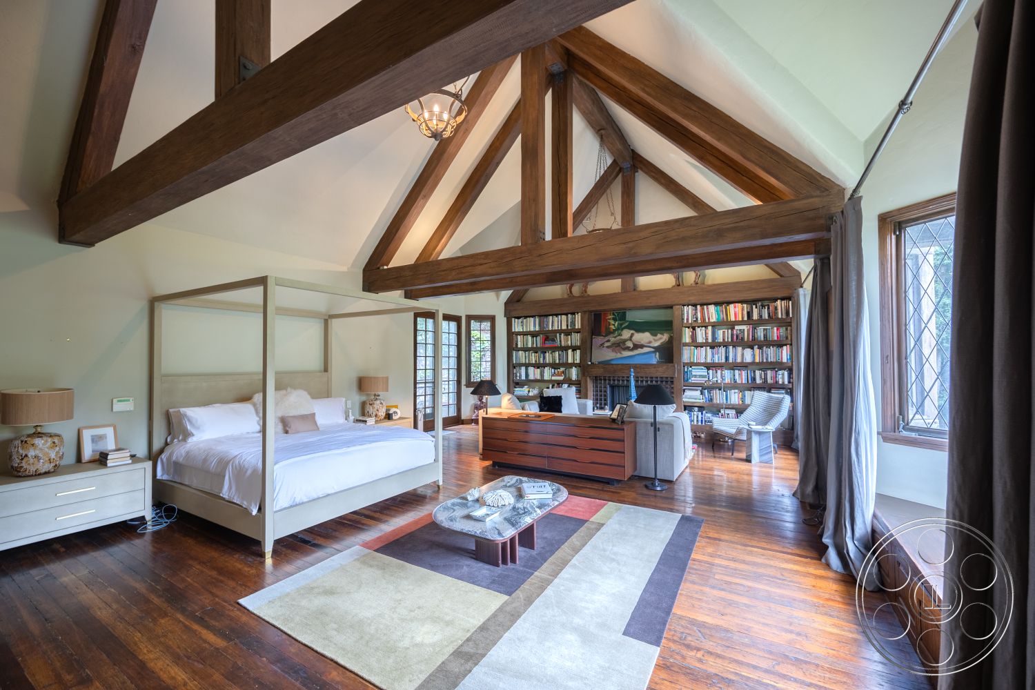 Mansion 2 - neutral color palette, artwork on wall, textured plaster walls, decorative coffee table, traditional architectural style, cozy reading nook, wood-framed windows, area rug with geometric pattern, exposed wood ceiling beams, natural light interior, hardwood bedroom floors, elegant chandelier lighting, canopy bed in master bedroom, large bay windows, library wall with built-in bookshelves, vintage table lamp, spacious interior layout, curtains providing soft light, glass door to outside, comfortable upholstered chairs