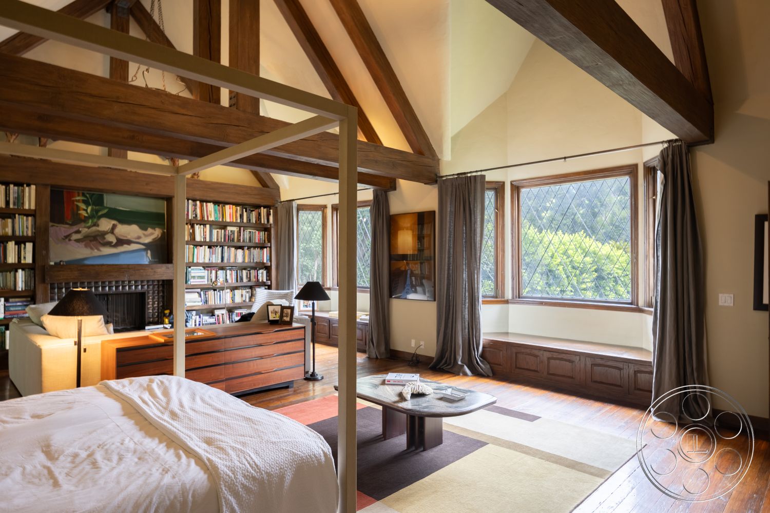 Mansion 2 - vaulted ceiling, textured plaster walls, comfortable seating area, craftsman architectural style, soft color palette, built-in bookshelves, light-filled space, exposed wood ceiling beams, hardwood bedroom floors, window seat with intricate woodwork, wood furniture accents, reading nook with large windows, interior room, painted accent wall, modern art decoration
