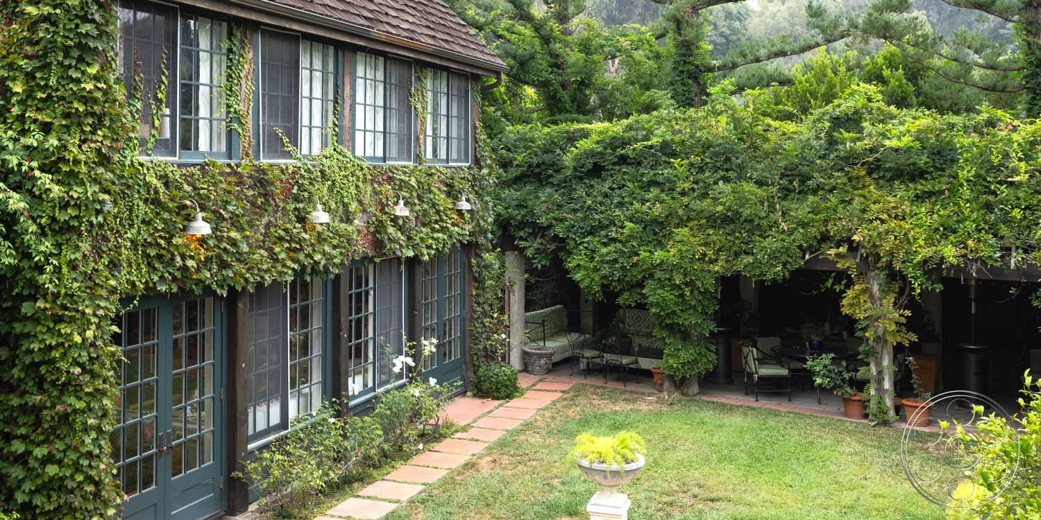 Mansion 2 - wooden window frames, cobblestone pathway, double-hung windows, outdoor lighting fixtures, shaded outdoor seating area, sloped roof design, exterior ivy-covered walls, landscaped garden with shrubs, outdoor decorative planters, traditional cottage style, stone patio tiles, rectangular backyard garden, exterior porch with wooden beams, surrounding green forest setting, textured wooden siding, lush garden foliage, brick garden edging