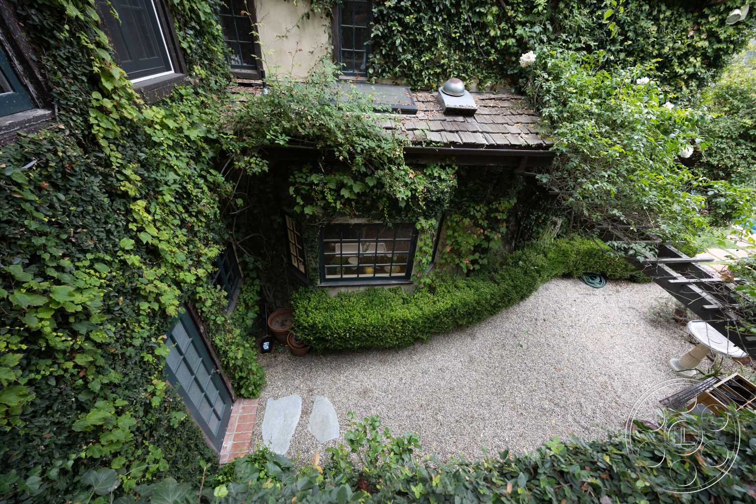 Mansion 2 - outdoor seating area, exposed brick walls, wooden window frames, ambient outdoor lighting, lush green landscaping, brick patio border, slate roof shingles, gravel garden path, landscaped garden beds, exterior ivy-covered walls, traditional cottage style, arched garden entrance, natural stone stepping stones, vegetation-covered facade, rustic wooden deck, courtyard garden setting, potted plants on window sills, scattered gravel flooring