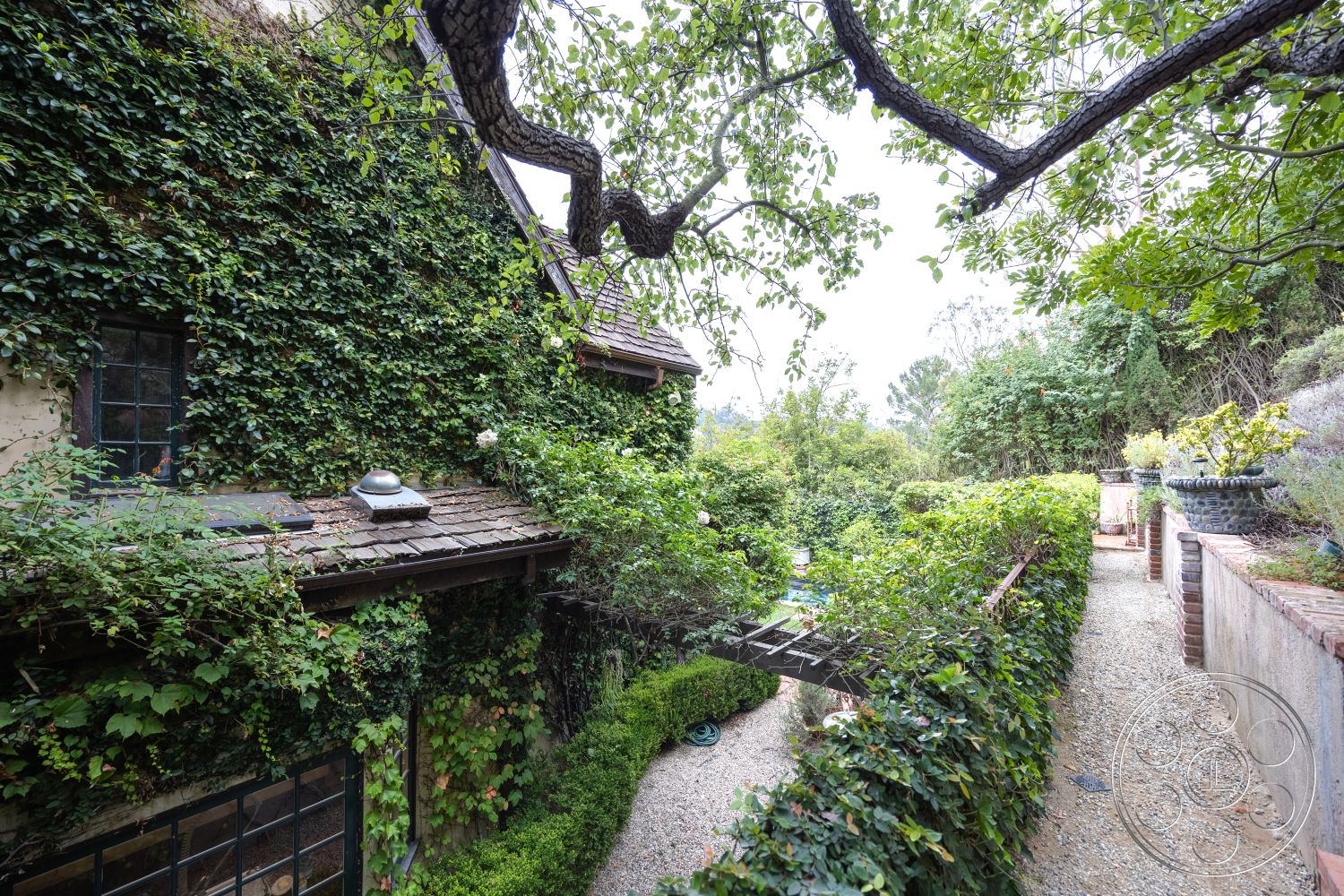 Mansion 2 - exterior, cobblestone patio, wooden window frames, ivy-covered walls, gravel path, slate roof, stone planters, brick garden wall, lush garden landscaping, rustic cottage style, wood trellis, mature trees surrounding, residential courtyard, suburban garden setting, natural stone wall treatment