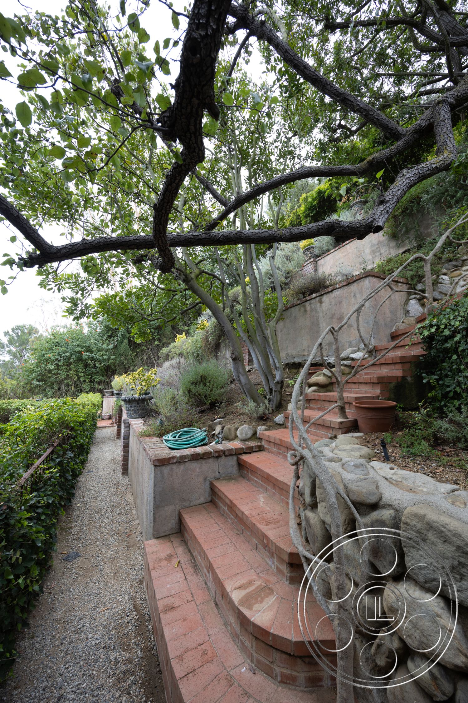 Mansion 2 - textured concrete path, landscaped garden setting, lush greenery landscaping, exterior brick steps, exterior stone wall, exposed rock landscaping, curved brick pathway, natural stone retaining walls, rounded brick stair treads, wooden railings on staircases, terraced garden design, oversized stone planters, irregular shaped stone accents, drainage gravel surface, nature-inspired outdoor staircase, country garden aesthetic