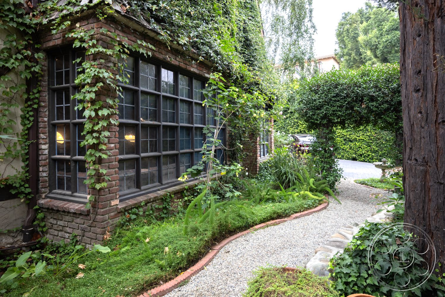 Mansion 2 - natural stone accents, paver driveway, outdoor seating area, gravel walkway, wooden fence, integrated outdoor lighting, lush green foliage, landscaped garden path, exterior brick wall, ivy-covered facade, exterior casement windows, vegetative trellis, brick border edging, circular garden bed, garden with native plants, multi-level greenery