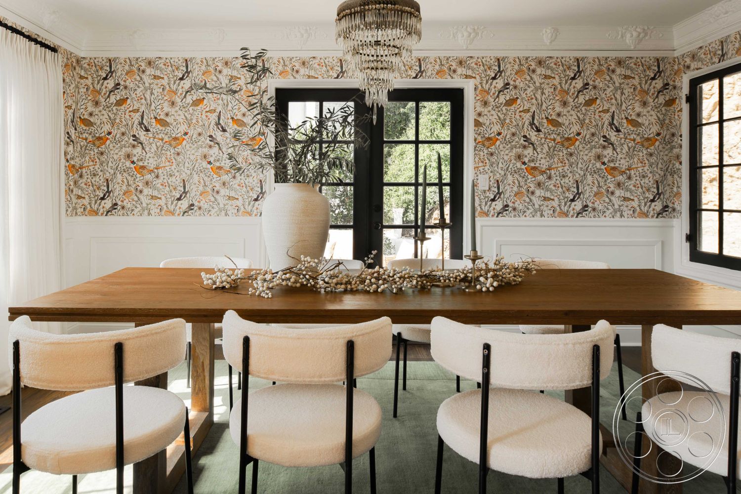 Spanish 166 - neutral color palette, upholstered dining chairs, wood dining table, floral wallpaper, floor-to-ceiling windows, chandelier lighting, modern farmhouse style, rustic decor elements, open dining area, natural light interior, plant decor accent, black steel chair legs, white crown molding, paneled wainscoting, large ceramic vase, decorative table centerpiece, textured wallpaper design, area rug flooring, sunlit dining space