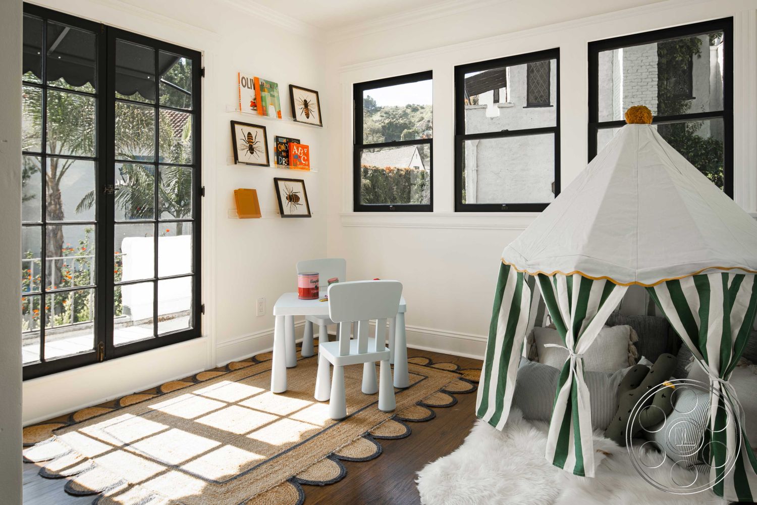Spanish 166 - natural light interior, decorative wall art interior, white painted walls interior, hardwood floor interior, minimalist decor interior, black steel framed windows interior, striped fabric play tent interior, beige area rug interior, children's play area interior, tan cushion seating interior, open view to outdoor space interior, textured ceiling paneling interior, playful design elements interior