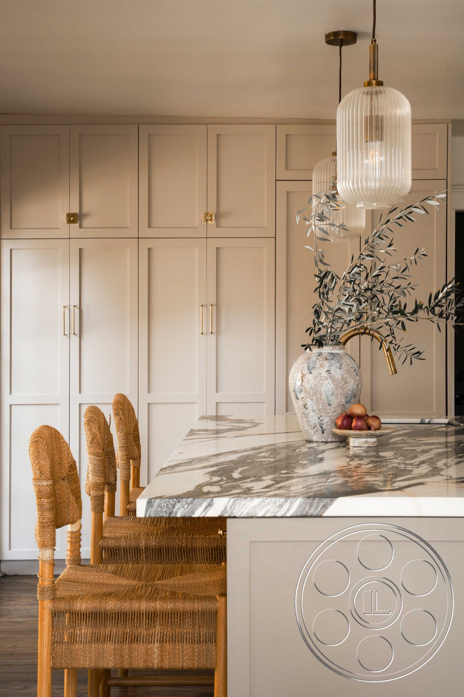 Spanish 166 - neutral color palette, pendant lighting fixtures, woven dining chairs, modern kitchen design, interior kitchen space, open kitchen layout, marble kitchen island countertop, minimalist kitchen decor, flat panel kitchen cabinets, gold hardware kitchen handles, wooden kitchen flooring, vase centerpiece with foliage, contemporary cabinetry, light-filled kitchen area, smooth countertop finish