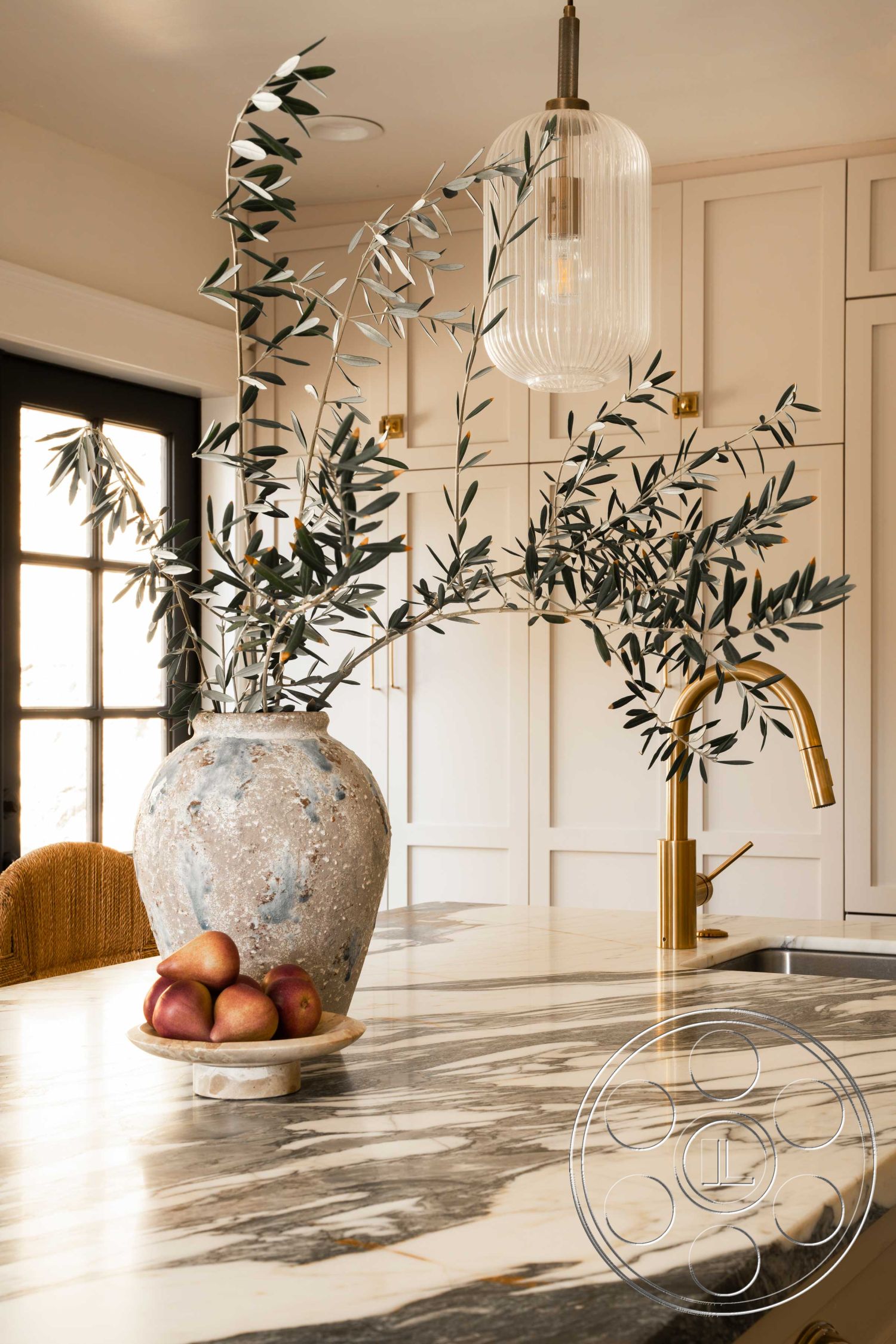Spanish 166 - interior neutral color palette, interior open kitchen layout, interior textured wall treatment, interior marble kitchen countertop, interior light wood cabinetry, interior glass pendant lighting, interior brass kitchen faucet, interior terracotta decorative vase, interior fruit display with apples, interior natural foliage decoration