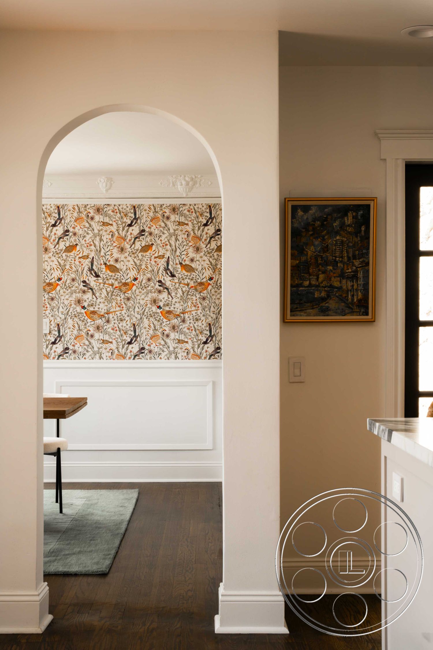 Spanish 166 - hardwood flooring, neutral wall colors, dining area, wood dining table, white wainscoting, arched doorway, floral wallpaper accent wall, classic crown molding, modern area rug