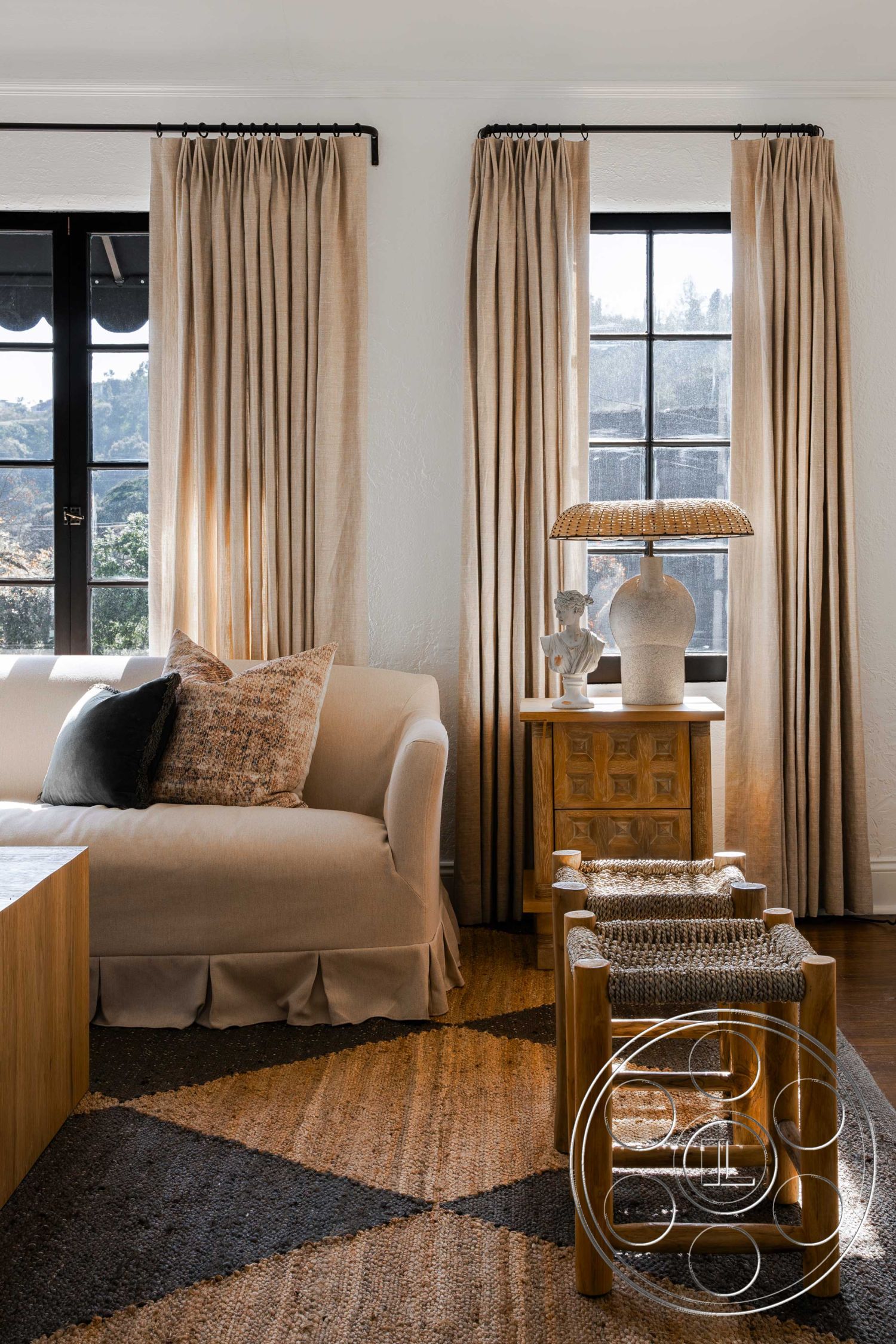 Spanish 166 - earthy color palette, city skyline view, black window frames, woven area rug, textured plaster walls, decorative throw pillows, geometric patterned rug, light wood coffee table, linen curtain drapes, beige upholstered sofa, wood accent side table, sculptural table lamp, natural wood stools, relaxed living room setting, artisan-style home decor