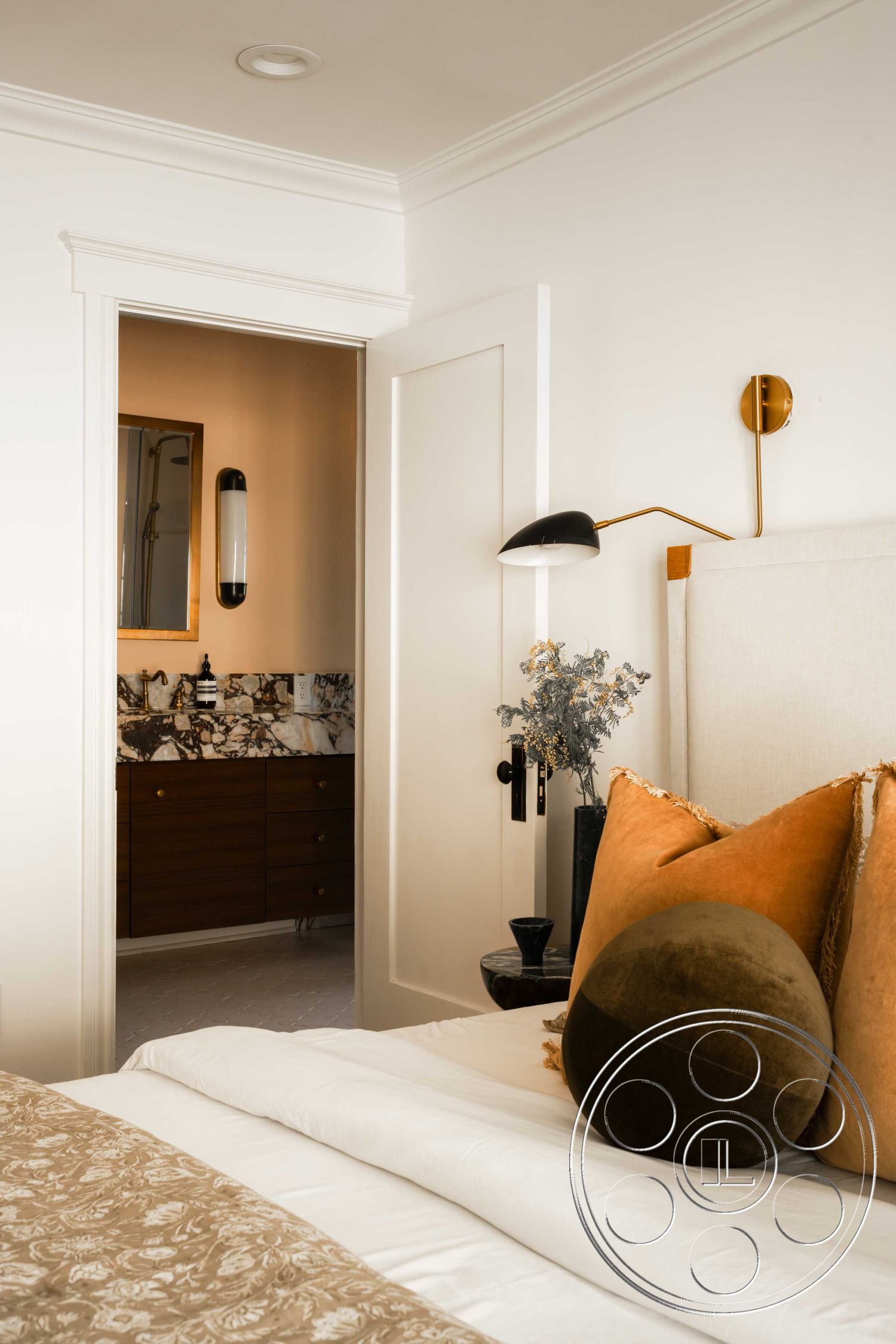 Spanish 166 - neutral color palette, minimalist design, inviting atmosphere, artistic wall decor, elegant light fixtures, walnut cabinetry, crown molding details, glossy tile flooring, cozy bedroom layout, open doorway to bathroom, soft-textured bedding, gold accent pillows, walled room with door, modern wall sconce lighting, marble bathroom countertop, decorative round pillow, engineered hardwood floor, subtle floral textures, contemporary bed frame