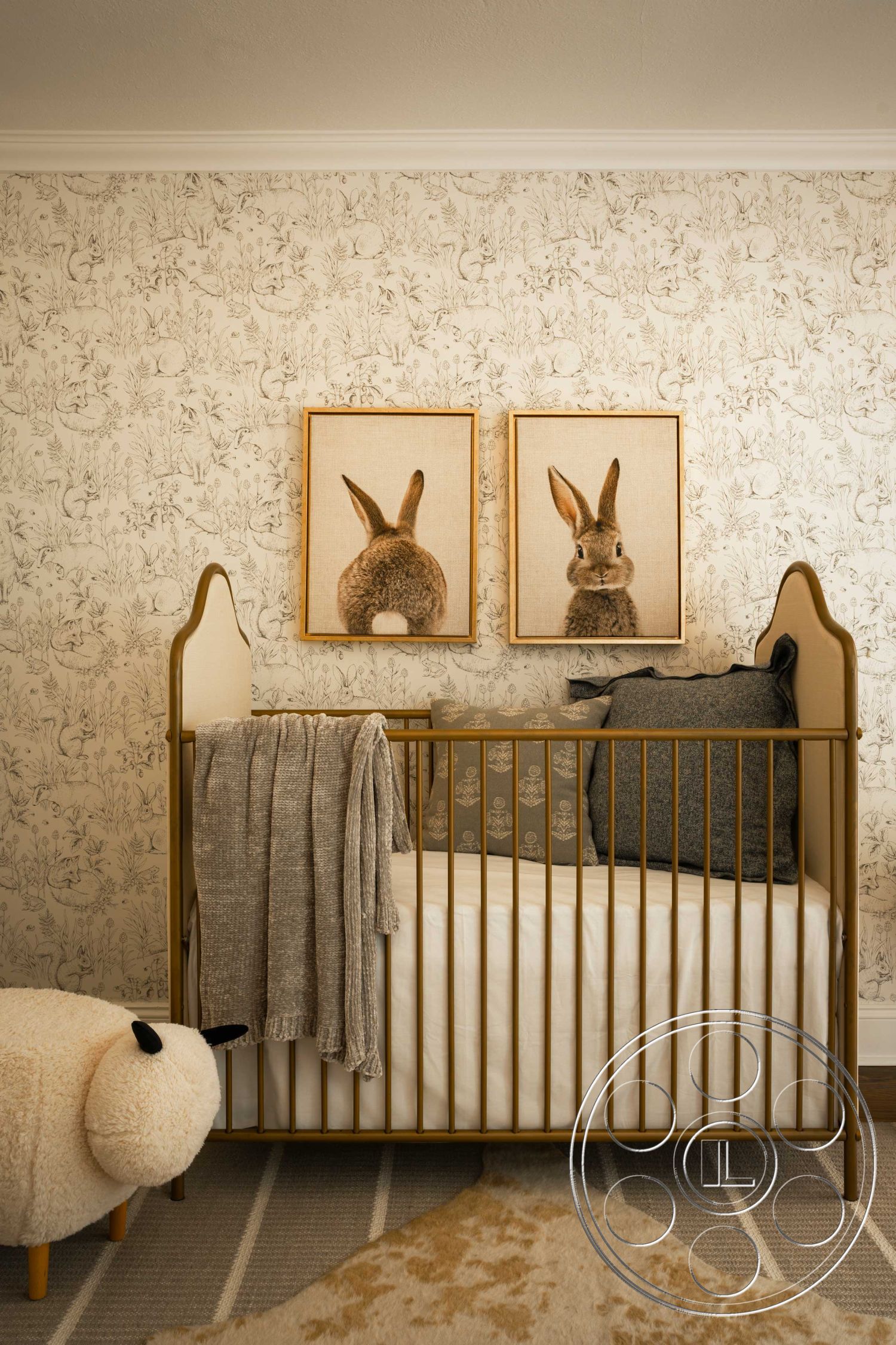 Spanish 166 - baby room, floral wallpaper, light wood flooring, textured throw blanket, soft area rug, crown molding details, interior nursery design, gold metal crib, art prints of rabbits, cream and beige color palette, plush decorative pillow, sheep-shaped ottoman, cozy children's space