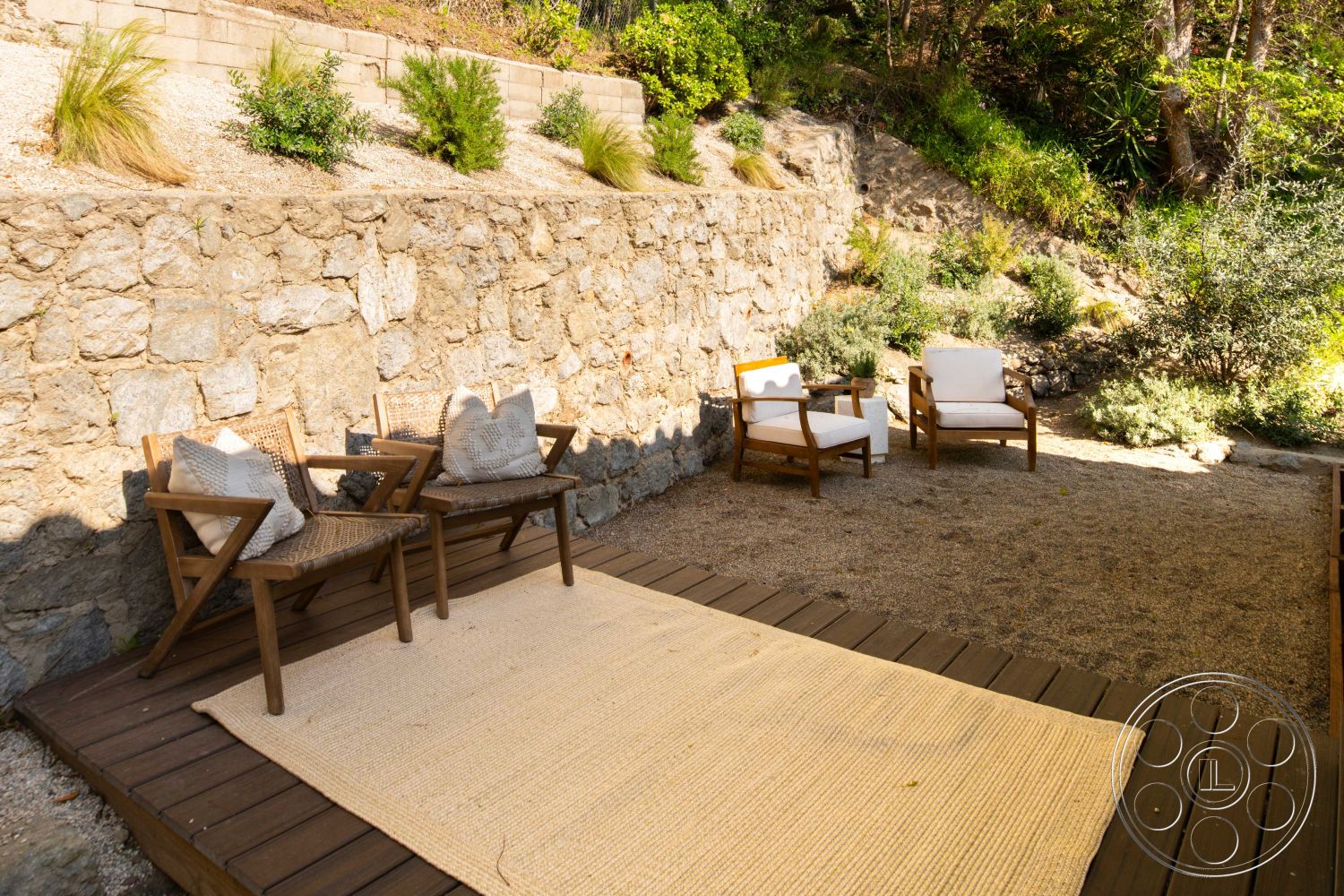 Spanish 166 - surrounding hillside, woven outdoor chairs, contemporary outdoor design, natural stone retaining wall, wooden deck flooring, environmentally integrated landscape, exterior stone wall, crafted wooden furniture, neutral outdoor rug, desert landscape garden, slots of greenery in urban setting, relaxed outdoor seating area, gravel patio surface, sunlit garden retreat, private backyard lounge