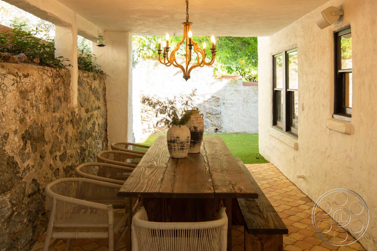 Spanish 166 - wood dining table, textured plaster ceiling, natural light from windows, hexagonal tile flooring, woven dining chairs, stucco wall finish, exposed stone wall interior, hanging chandelier lighting, sunlit indoor patio area, plants in decorative vases, rustic dining space, outdoor-indoor transitional area, bottom-up view of surrounding greenery, handcrafted wooden furniture, elevated patio setting