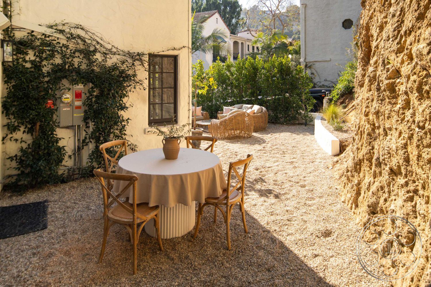 Spanish 166 - ivy, sunlit terrace, natural stone wall, circular dining table, wooden dining chairs, modern light fixture, exterior patio, urban garden setting, lush plant landscaping, gravel outdoor flooring, fabric tablecloth, built-in greenery, cozy outdoor seating area, textured rock formation, relaxed dining area, private courtyard ambiance