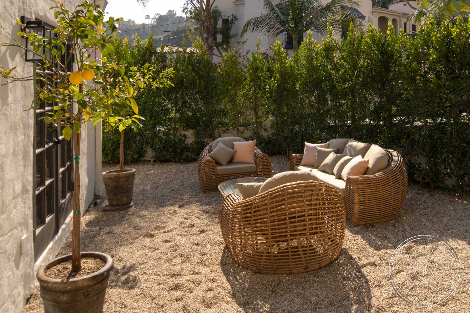 Spanish 166 - Outdoor Furniture, tropical landscaping, hedge privacy wall, gravel patio flooring, cozy outdoor lounge area, white stucco exterior walls, woven rattan outdoor seating, comfy throw pillows, framed black window details, potted citrus tree, sunny garden setting, interior garden retreat, relaxed outdoor living space