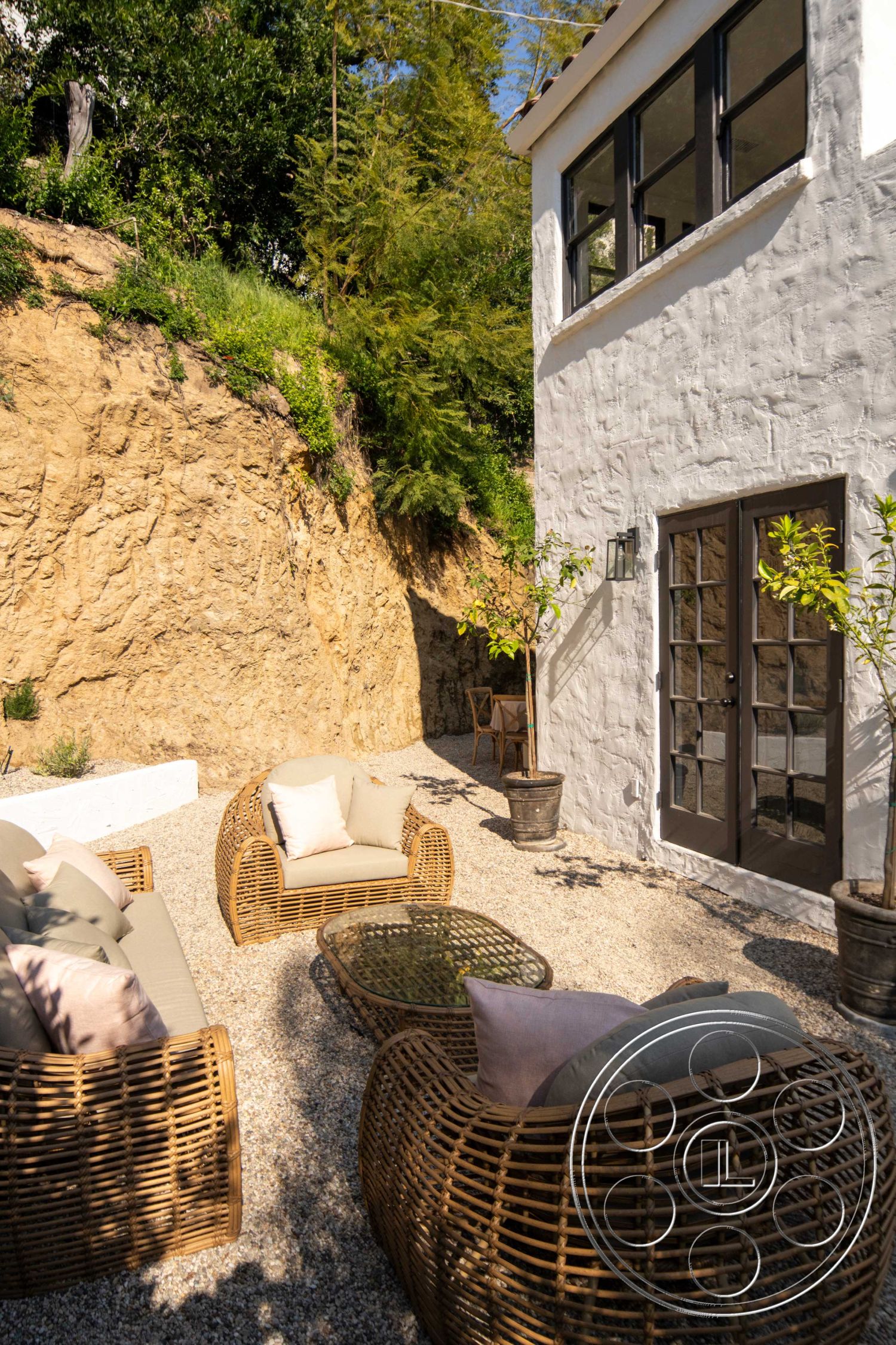 Spanish 166 - Outdoor Furniture, exterior, glass coffee table, outdoor lounge area, landscaped garden, indoor-outdoor flow, stucco walls, floor-to-ceiling windows, gravel patio flooring, planter pots with greenery, natural hillside setting, woven rattan outdoor chairs, wooden door with glass panels