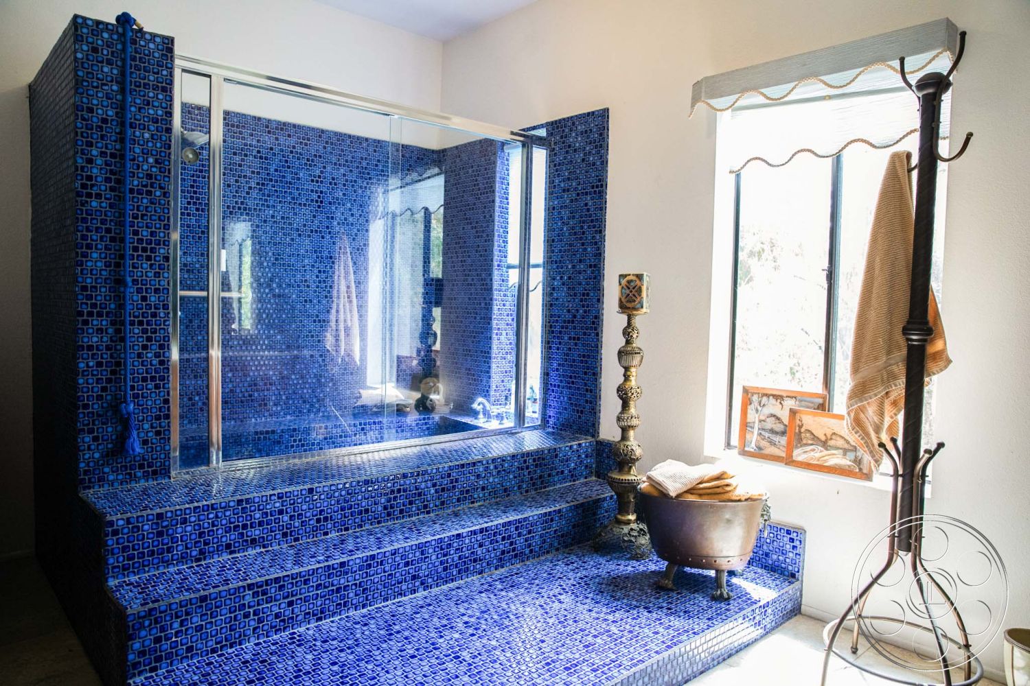 Medit 31 - glass shower enclosure, textured ceiling, natural light from windows, interior bathroom, minimalist towel rack, blue ceramic tile shower walls, blue ceramic tile shower floor, studded threshold step, contemporary freestanding bathtub, vintage brass floor lamp, decorative candle holder, warm wood accent window frames