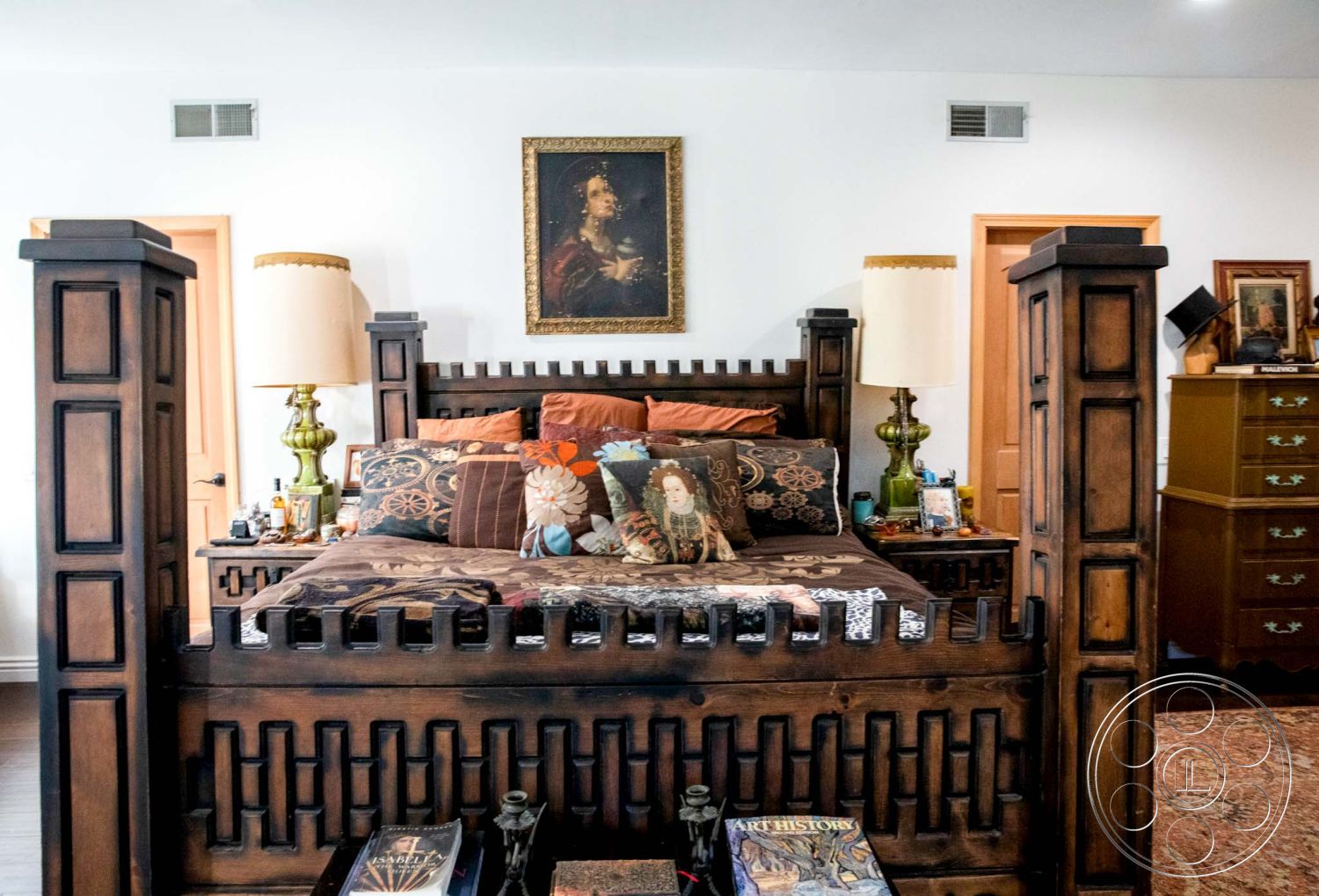 Medit 31 - textured wall art, dark wood furniture, ornate wooden bed frame, natural light from window, interior bedroom, hardwood bedroom floors, neutral painted walls, gold-framed mirror, exposed wooden door frames, colorful decorative pillows, vintage lamps with green bases, wooden dresser with vintage knobs, intricate tapestry bed cover, traditional portrait artwork, accent pillows with floral patterns, decorative books on nightstand, lamps with fabric shades, traditional rug flooring, cozy and eclectic decor