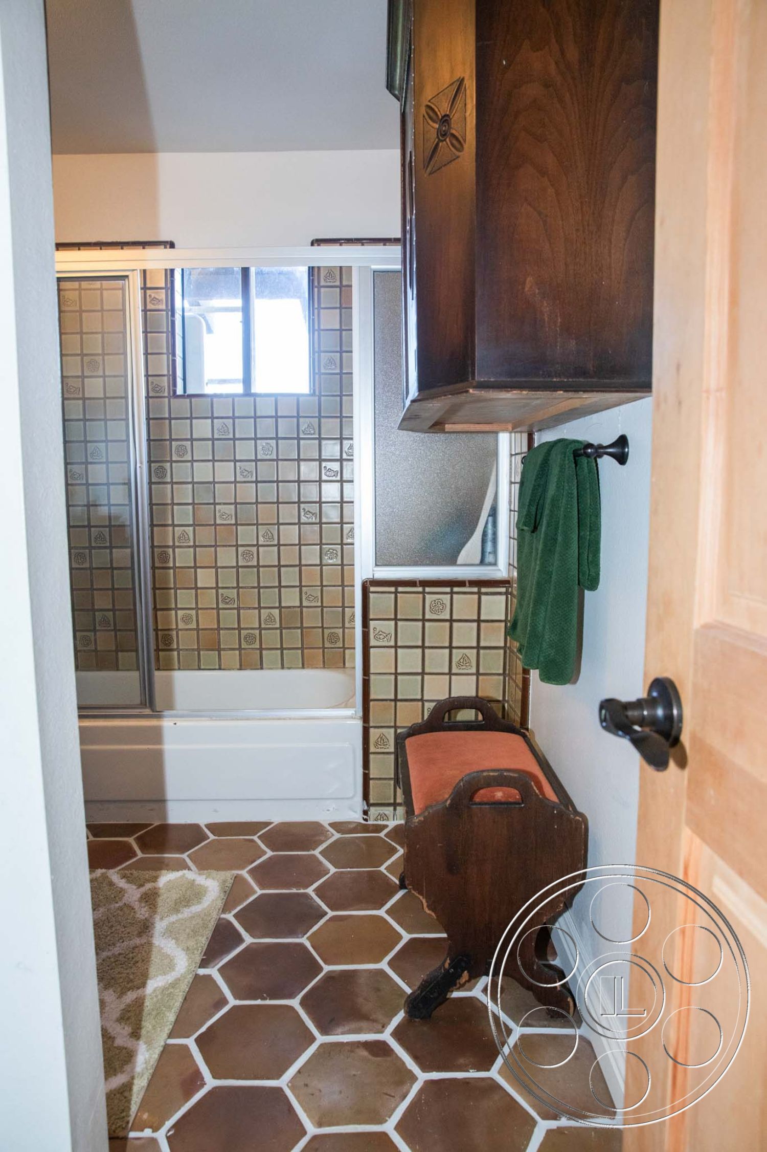 Medit 31 - dark wood cabinetry, neutral wall colors, glass shower enclosure, natural light from window, interior bathroom setting, vintage wooden bench, hexagonal tile bathroom flooring, textured wall tiles in shower area, built-in bathroom storage, green towel accents, modern bathroom decor, functional bathroom layout