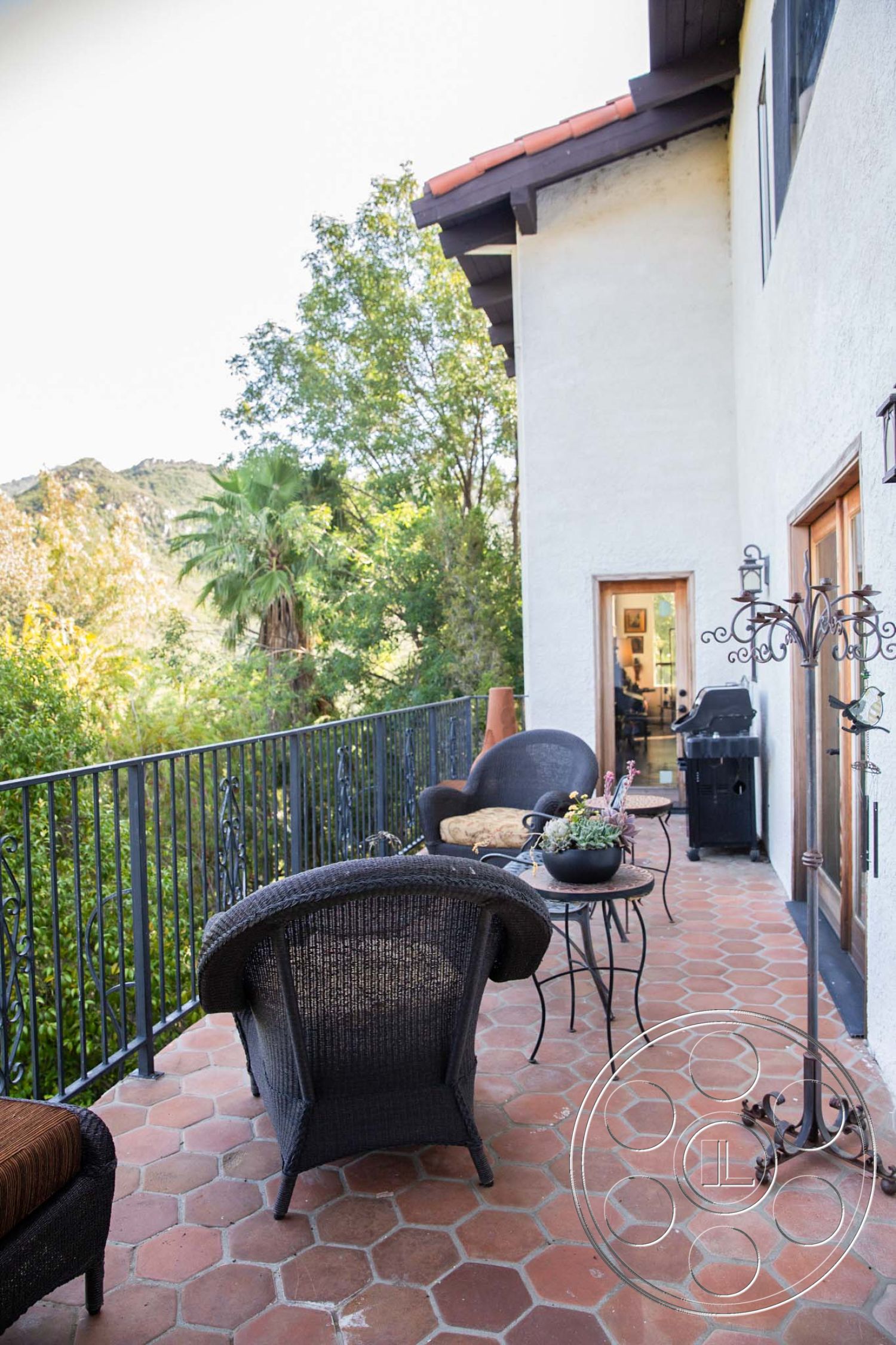 Medit 31 - outdoor dining area, lush greenery view, sunlit exterior, urban hillside location, mountain backdrop setting, hexagonal terracotta patio flooring, wrought iron balcony railing, Mediterranean-style exterior, textured stucco wall finish, overhang roof with red tile shingles, outdoor seating area with wicker chairs, ceramic planter for outdoor decor, exterior door leading into living space, porch area with metal table, patio surrounded by trees, interior access with glass doors