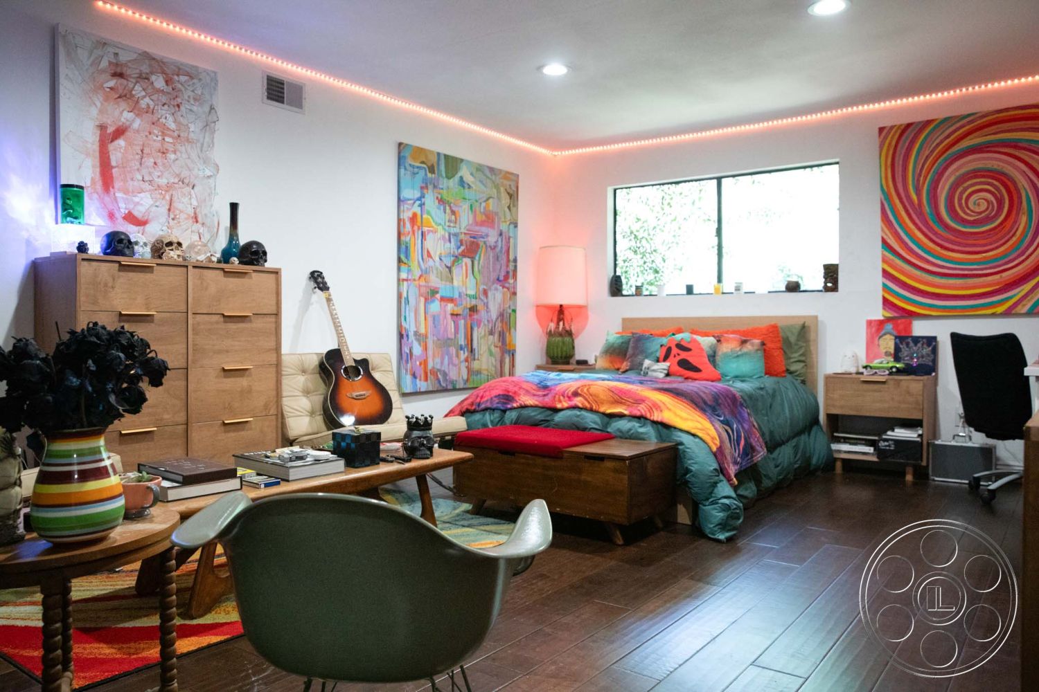 Medit 31 - open layout, modern art wall decor, multicolored area rug, hardwood bedroom floors, ambient LED lighting, colorful bedding set, wood dresser with gold hardware, bedside table with lamp, guitar as interior decor, wall-mounted window with natural light, abstract swirl painting, accent chair with mid-century modern design, decorative skull accents, books and decorative items on coffee table, floating nightstand, textured wall with neutral paint, casual and vibrant atmosphere