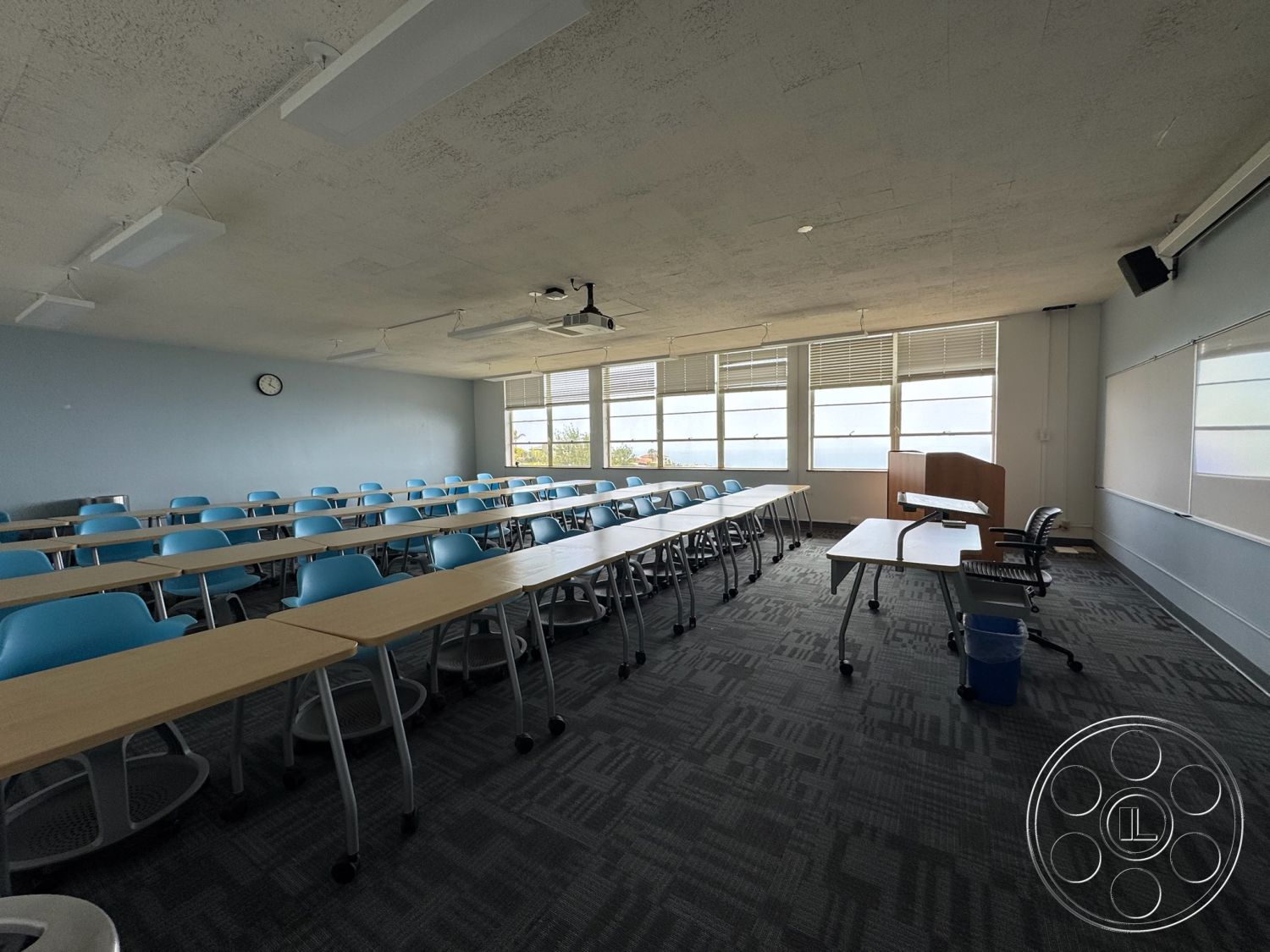 School 1 - natural light from windows, modern educational space, acoustic ceiling tiles, textured carpet flooring, concrete ceiling finish, hardwood classroom tables, blue plastic chair seating, glass window wall, whiteboard teaching wall, steel chair frames, interior classroom setting