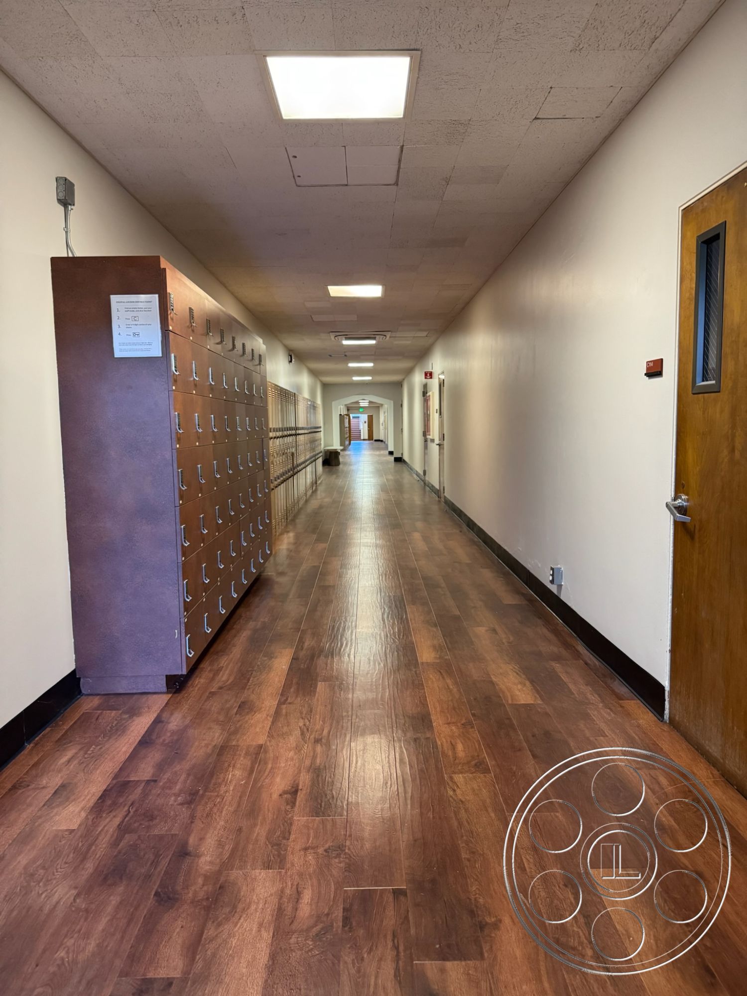 School 1 - white painted walls, linear hallway layout, exposed ceiling tiles, interior hallway design, laminate hallway flooring, metal locker storage, wooden door with glass insert, modern flush ceiling lights, school corridor, functional classroom entrance