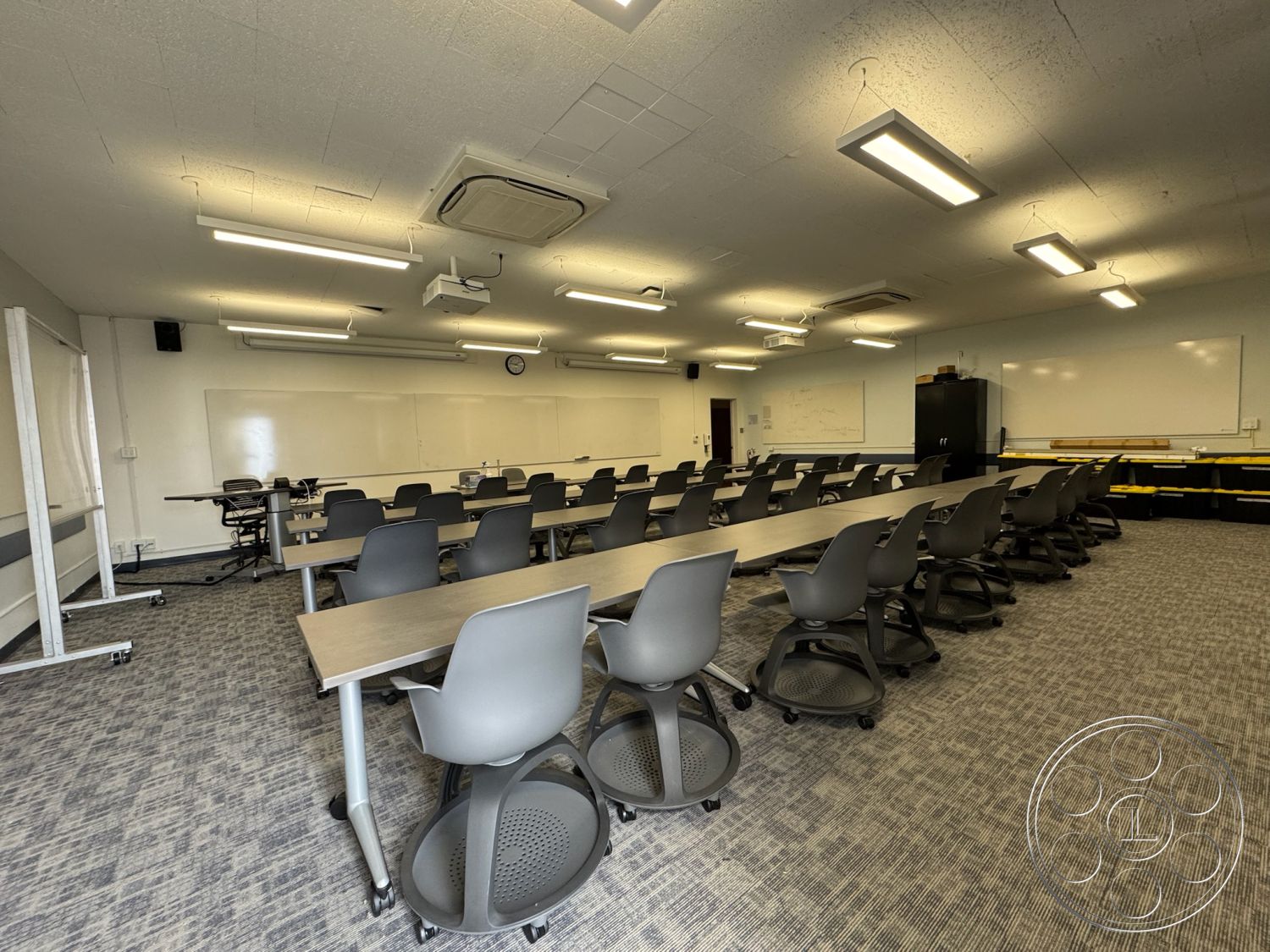 School 1 - neutral color palette, wall-mounted projector, acoustic ceiling tiles, LED overhead lighting, interior classroom design, carpet tile flooring, light gray textured carpet, modular classroom tables, rolling chairs with ergonomic design, whiteboard wall surfaces, black cabinetry for storage, open layout educational space