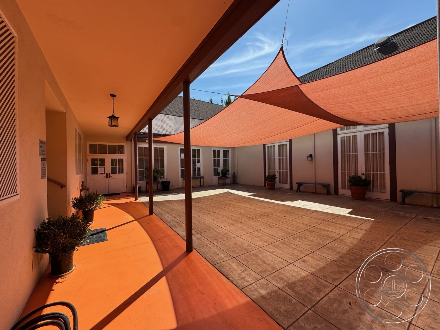 Spiritual Center - natural light, potted plants, exterior space, outdoor gathering space, decorative outdoor seating, white painted walls, urban courtyard setting, shaded outdoor area, painted concrete patio floor, textured orange sunshade, wood beam overhead support, framed glass double doors, slate tile courtyard area, light fixture hanging from ceiling