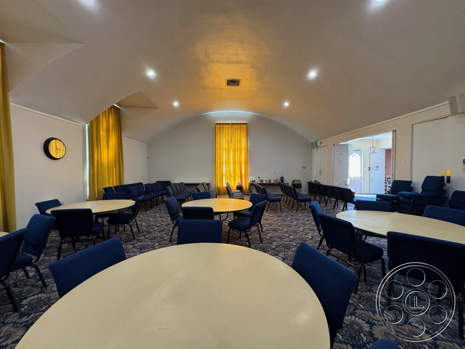 Spiritual Center - neutral color palette, modern light fixtures, interior space, carpet flooring, vaulted ceiling, textured plaster walls, blue upholstered chairs, circular tables, community gathering area, accessible entryways, acoustic ceiling, open room layout, yellow curtains, round decorative mirror