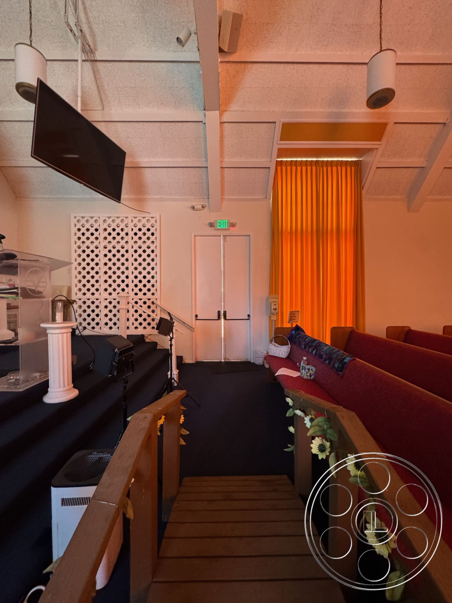 Spiritual Center - air conditioning unit, dark carpet flooring, acoustic wall treatment, glass podium, interior church space, wooden stage steps, panelled ceiling with exposed beams, orange sheer curtains, white synthetic lighting fixtures, red upholstered pews, decorative wood partition wall, modern audiovisual equipment, entry double doors, floral decorations