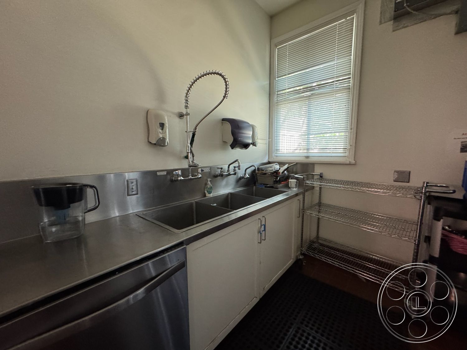 Spiritual Center - interior kitchen, white painted walls, stainless steel countertop, stainless steel commercial sink, high-efficiency faucet, glass window with blinds, industrial shelving unit, rubber floor mat, kitchen workspace