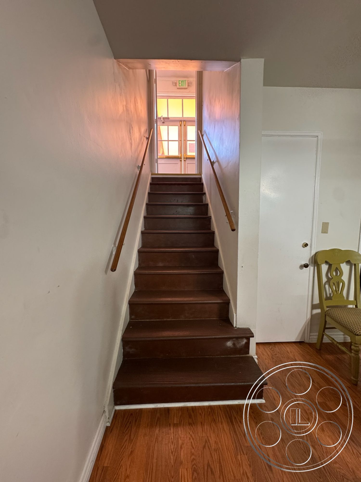 Spiritual Center - white painted walls, interior staircase, dark hardwood stairs, simple wooden handrail, natural light from doorway, open design hallway, brown wooden floor, brightly lit entrance, modern transitional style