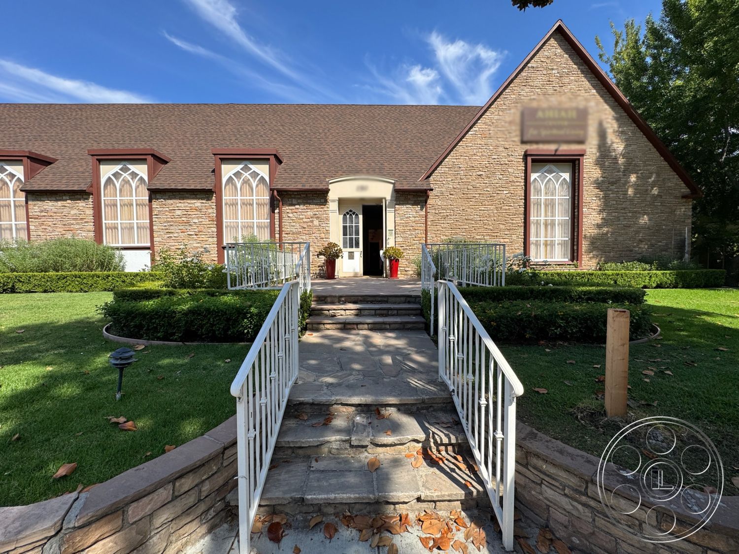 Spiritual Center - curved pathway, boxwood hedges, dormer windows, flagstone walkway, wrought iron railings, traditional home design, landscaped garden beds, arched window frames, gabled roof with asphalt shingles, exterior stone veneer walls, smooth concrete steps, brick exterior chimney, door with decorative trim, stone faÃ§ade accents, planting beds with seasonal flowers, flush-mounted outdoor lighting, sloped front lawn