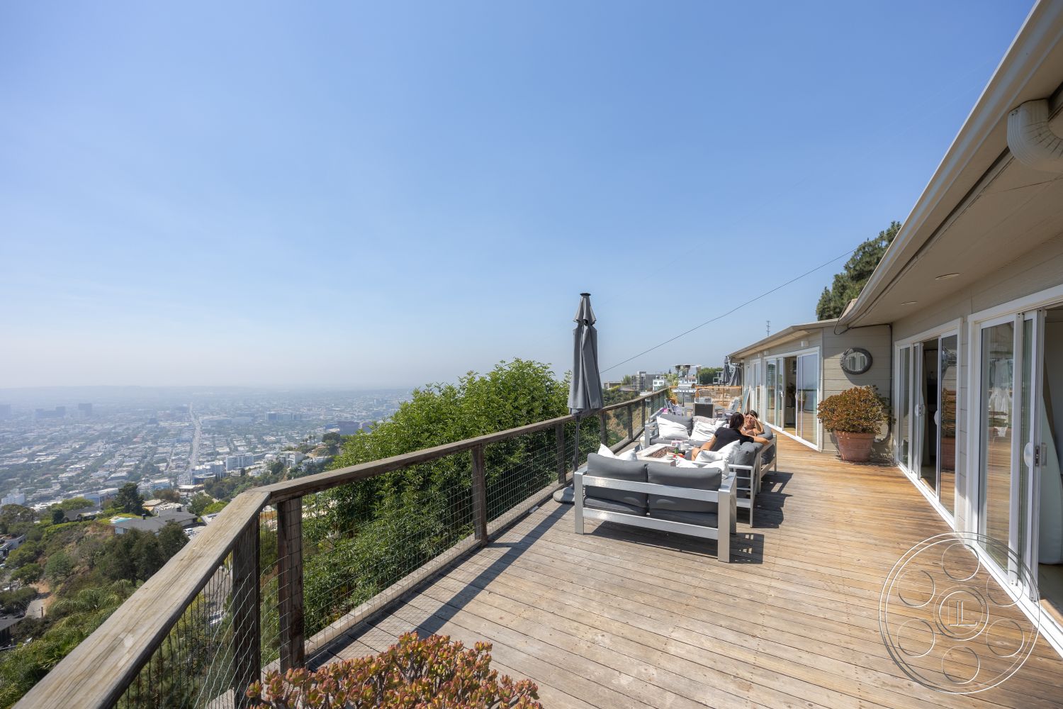 Retro 294 - glass sliding doors, city skyline view, sustainable landscaping, outdoor lounge seating, wood deck patio flooring, open-air entertainment area, sunny hillside location, metal railing fence, natural landscape backdrop, modern exterior design