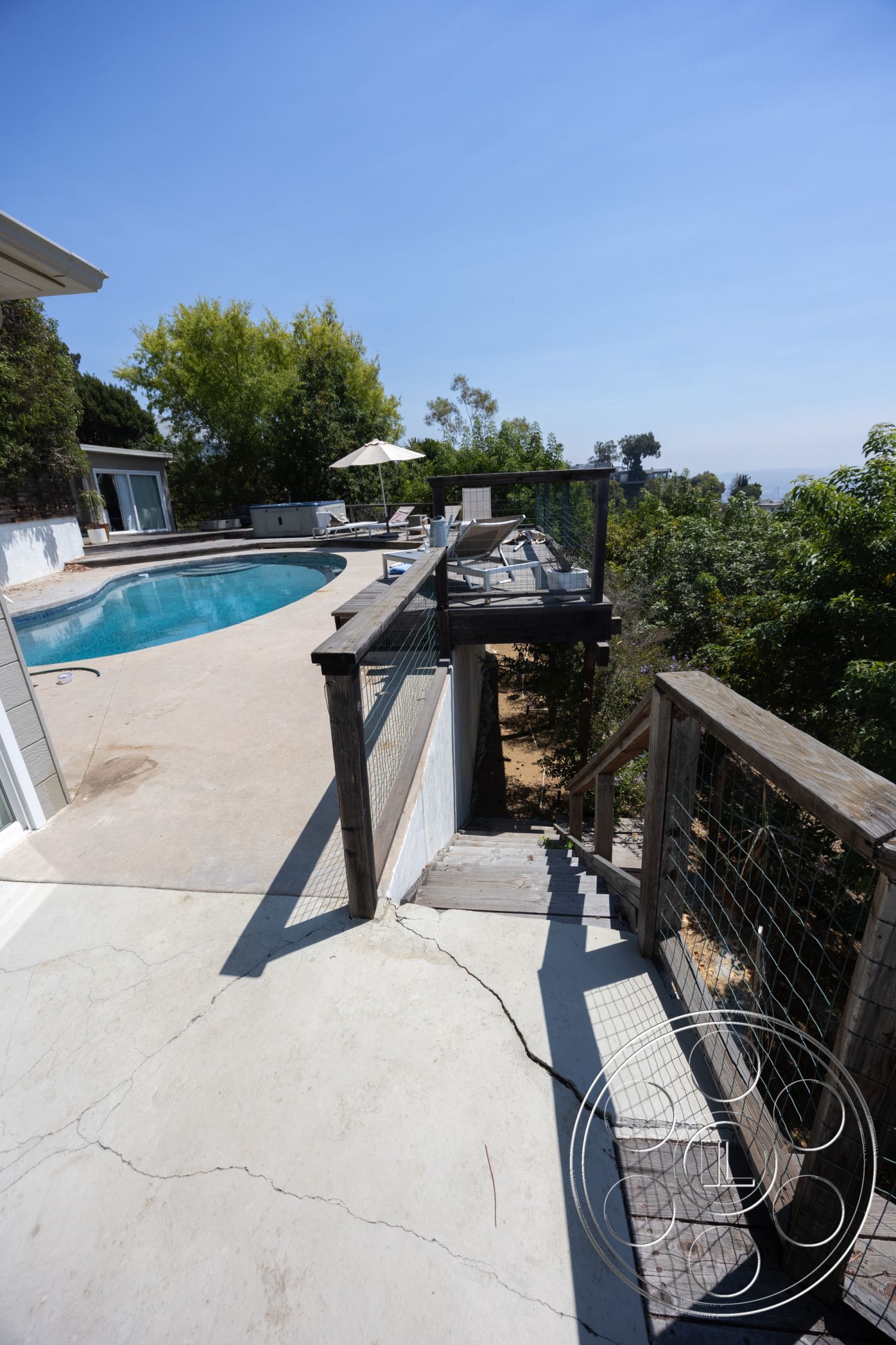 Retro 294 - surrounding greenery, landscaped backyard, open outdoor space, city skyline view, oval swimming pool, concrete patio floor, exterior concrete pool deck, modern outdoor living area, sunny hillside location, wooden stair railing, wooden step stairs, metal mesh fencing